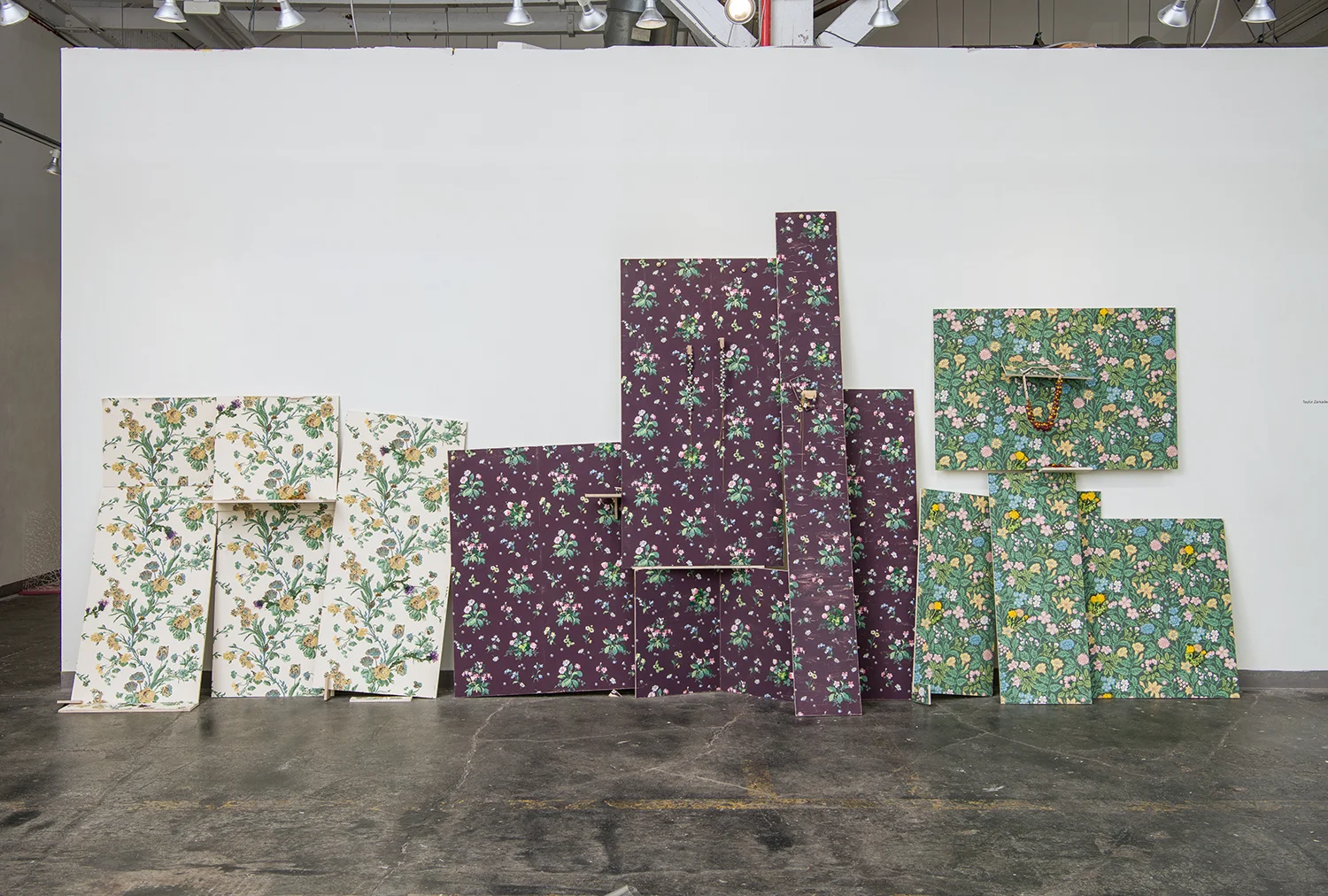 Lay it on Thick / 2018 Lay it on Thick is an imagining of possibility, assembled narratives, and the subtle support structures that aid in identity formations. The installation gestures to three curling photographs affectionately leaning into one another, the individuals in the frames identified by jewelry objects that find rest on several panels. The stability of the stacked panels rely on strangely cast bronze bolts in various states of becoming, and cut scraps from the installation that seem to add complication but play an important role in the overall balance of the piece— both tests of trust in relationship and kinship. Through thinly veiled strategies of camouflage, intimate moments are slightly obscured to slow the visual experience of the work— to encourage lingering and reward patience. Nothing is completely hidden, but it is not always given readily— and not always so easily understood. Materials / Wood, scraps, wallpaper, aluminum, silver, bronze, 14k gold, nylon, sequin pins, screws, reflective glass beads, crayon, wildflowers that are weeds, heat