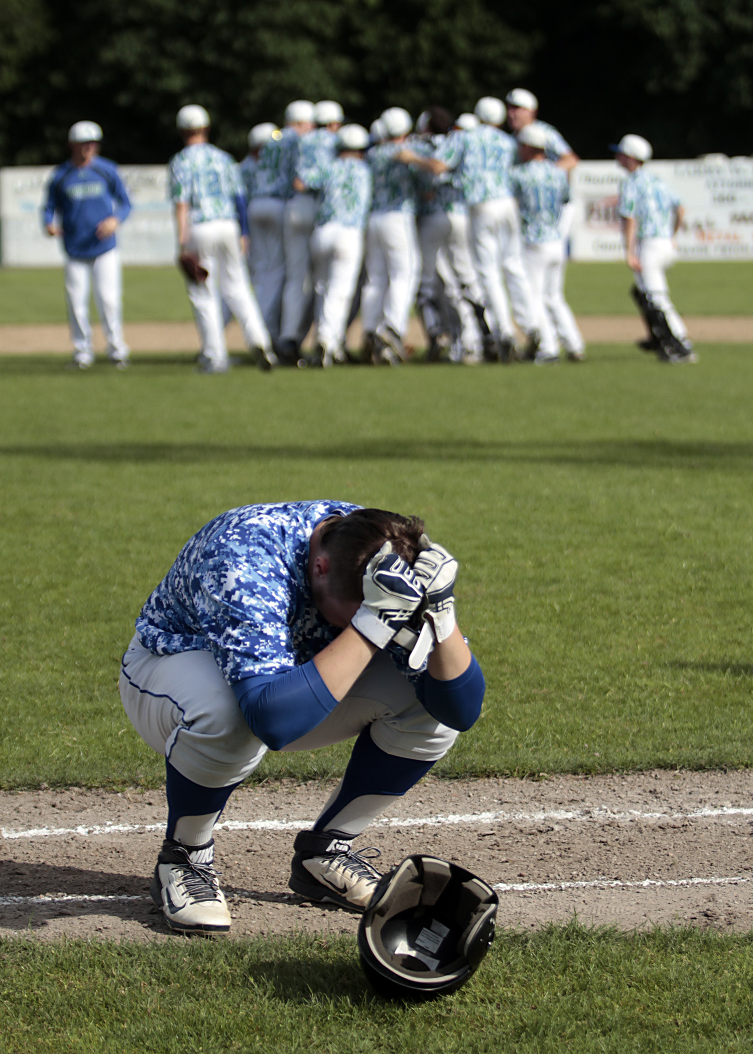  Trent Schulte, of Bainbridge High School, crouches near the dugout&nbsp;visibly upset following the varsity baseball team's 1-0 loss in the second game of the 2013 State Tournament. The victorious team from Shorewood High celebrates in the backgroun