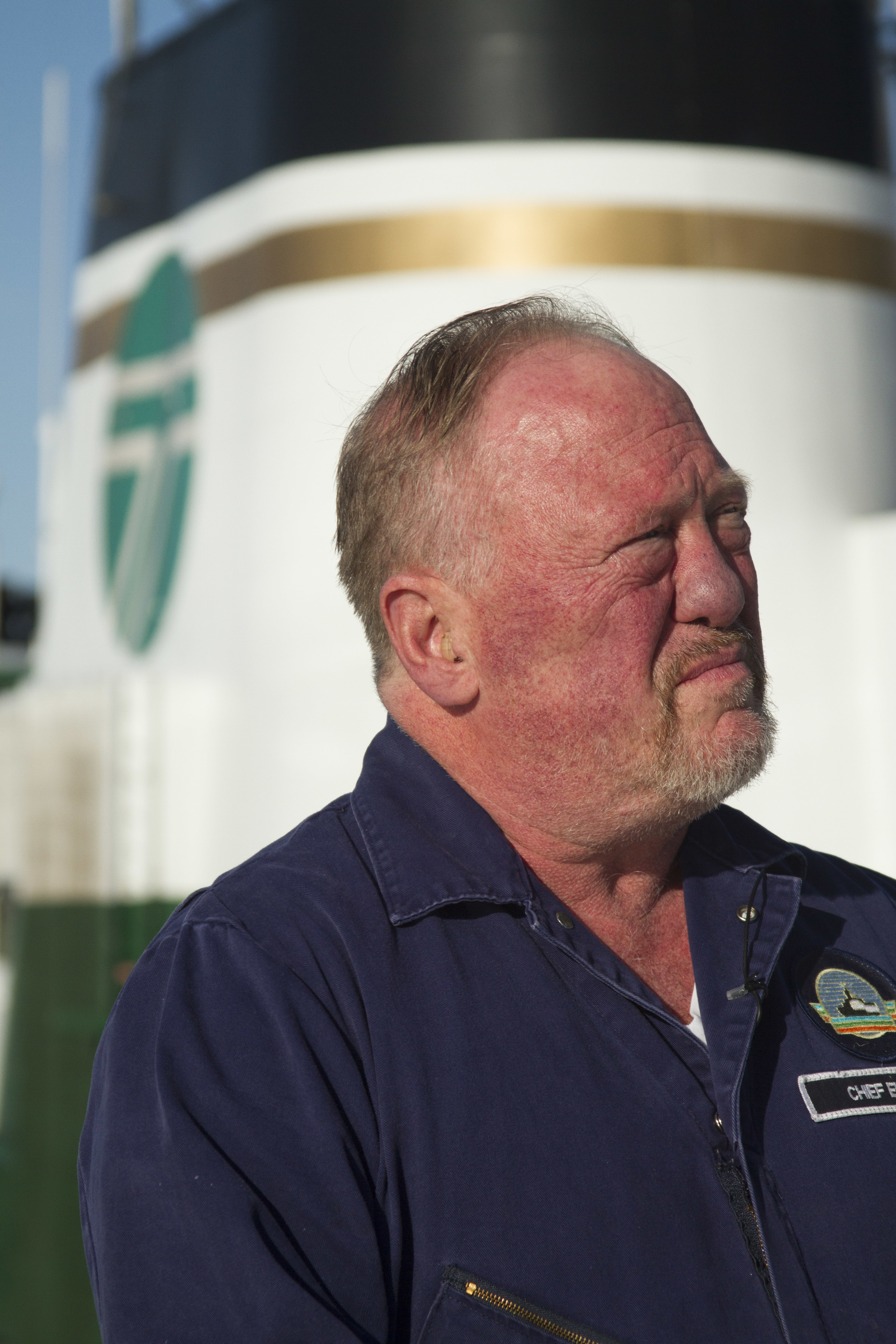   Mike Fagernes, the M/V Evergreen State’s last chief engineer, stands before the stack on the sun deck, which is adorned with the gold band awarded all vessels with 50 years of service.  