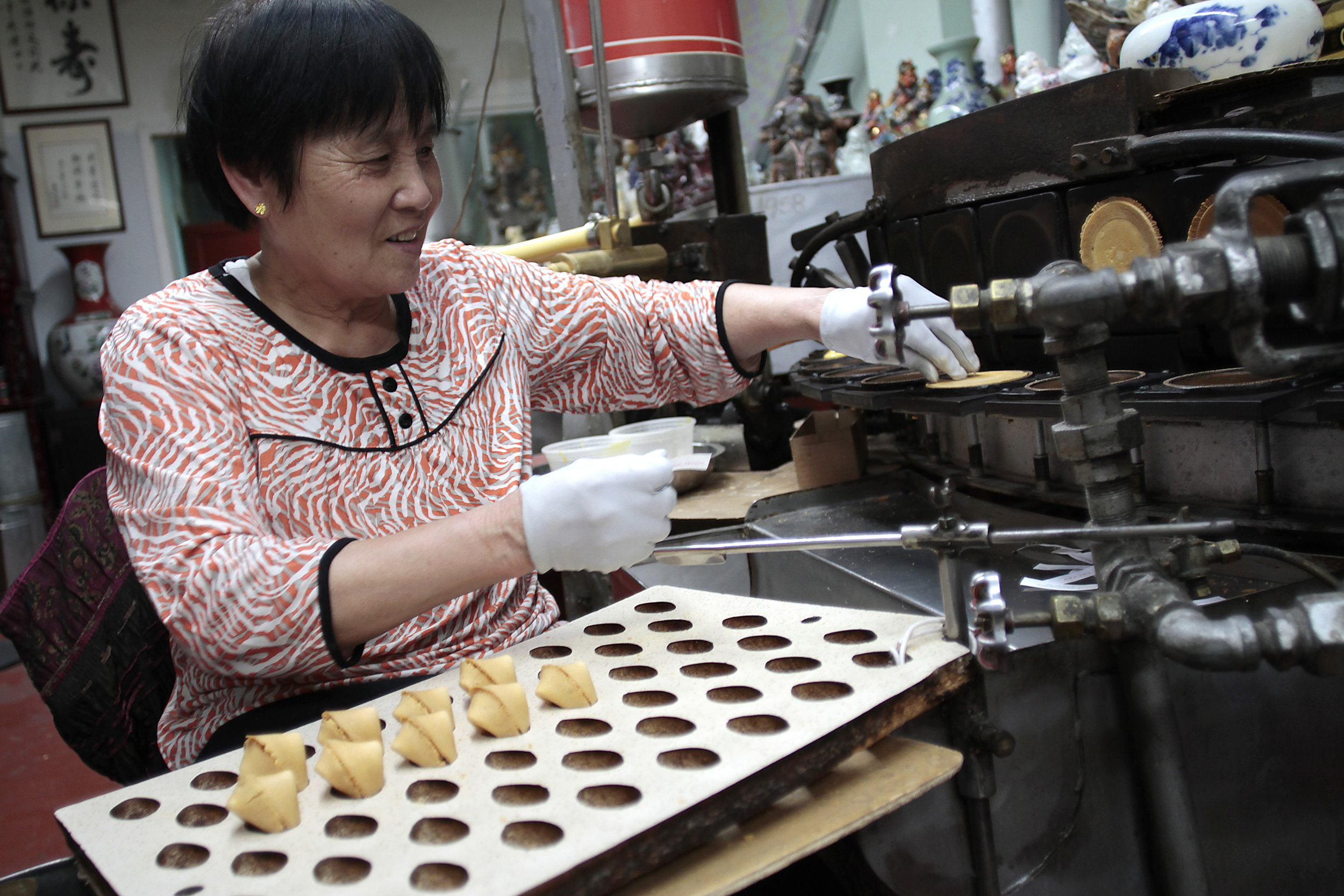 A woman folds fresh fortune cookies into shape around the tiny slips of paper at the famed Golden Gate Fortune Cookie Company in San Francisco, Sept. 2017. 
