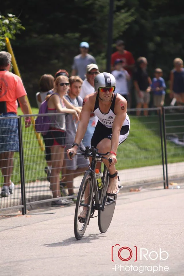 This shot was taken just before entering T2. They had moved the mount/dismount line back about 100 meters from where we started so I swung my leg off the bike way too soon resulting in me having to ride my bike in like skateboard, with one foot on the pedal and one pushing off the ground. Photo Credit: Robert Mahaits