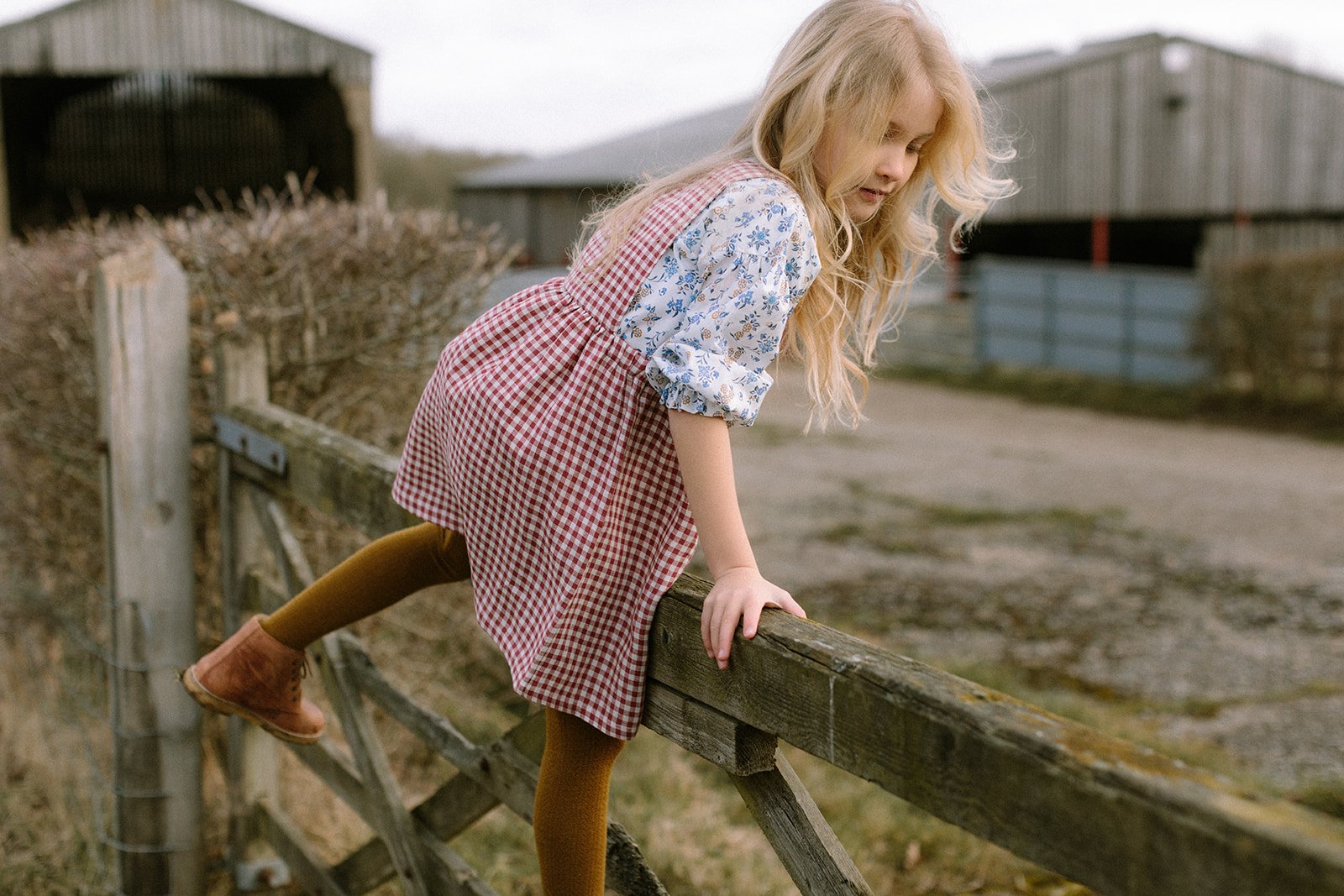  childrenswear fashion photographer girl on farm gate in red linen gingham dress 