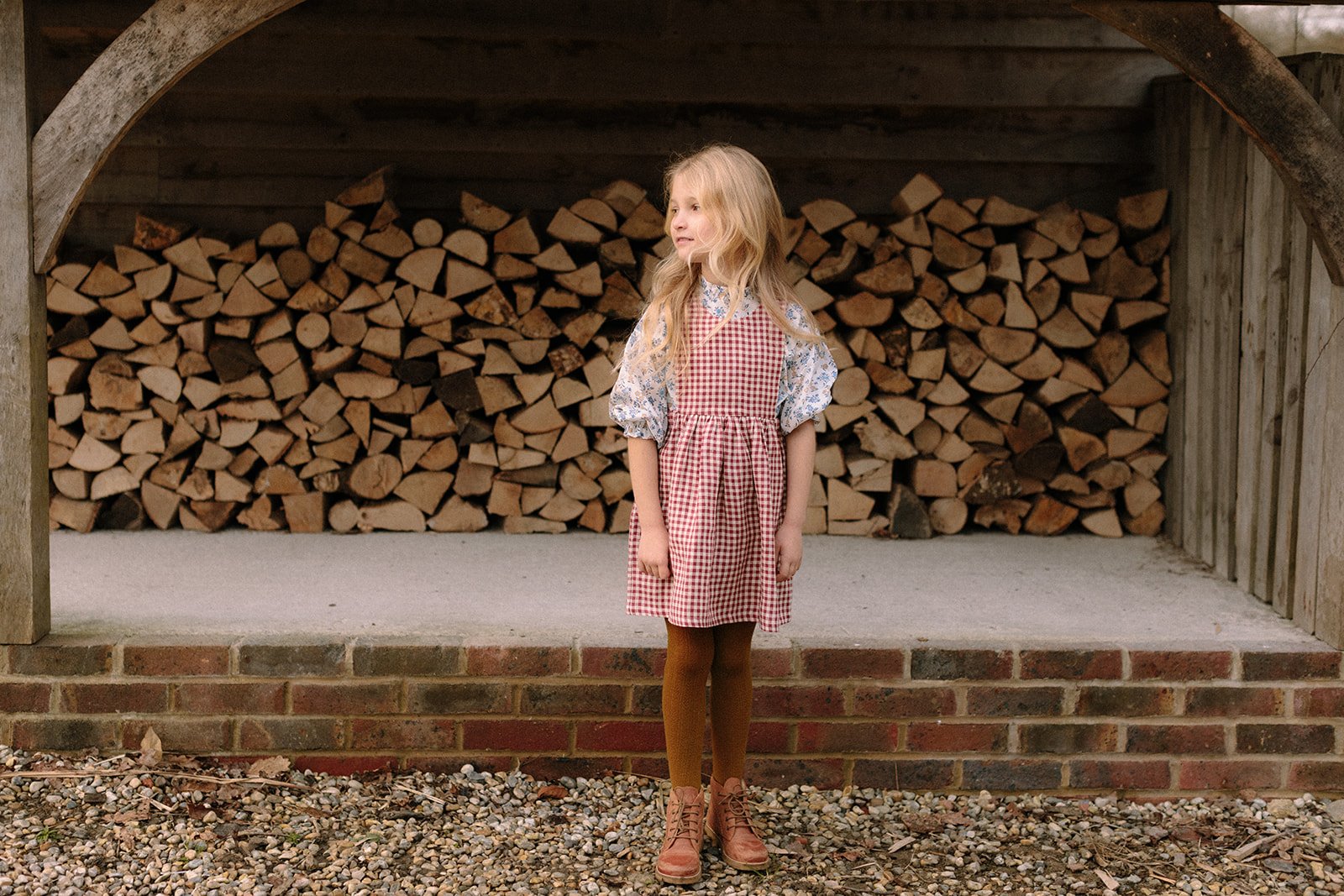  childrens fashion photographer girl in red gingham dress in front of logs 