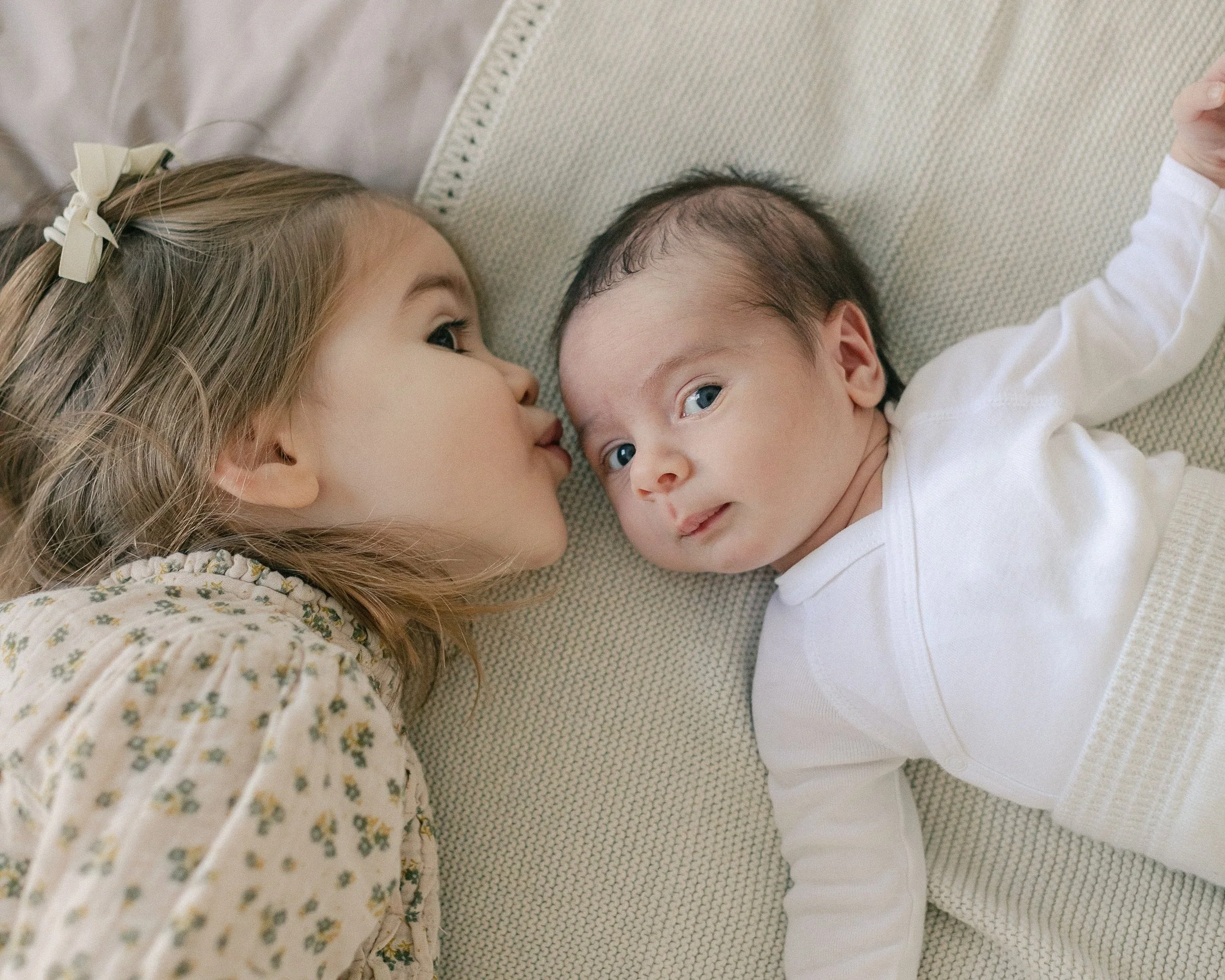 Older sister kissing her newborn sibling during a relaxed Tunbridge Wells home newborn photography session