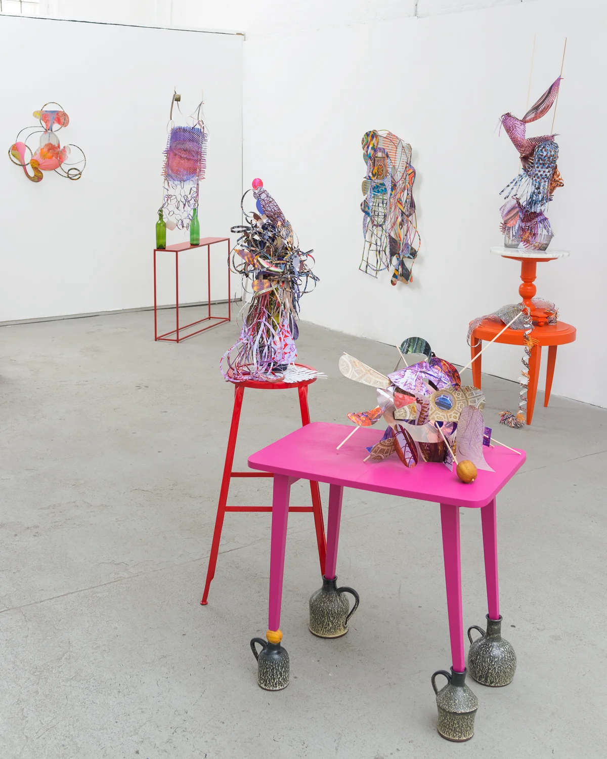  from left to right:   Feverish follies , 2013  cut-up inkjet prints, 26 x 26 inches   Beebalm-sunburst-ballet , 2014  cut-up inkjet prints, Polaroid, c-print, red metal table, wooden dowels, miniature clothespins, and glass bottles, 76 x 38 x 8 inch