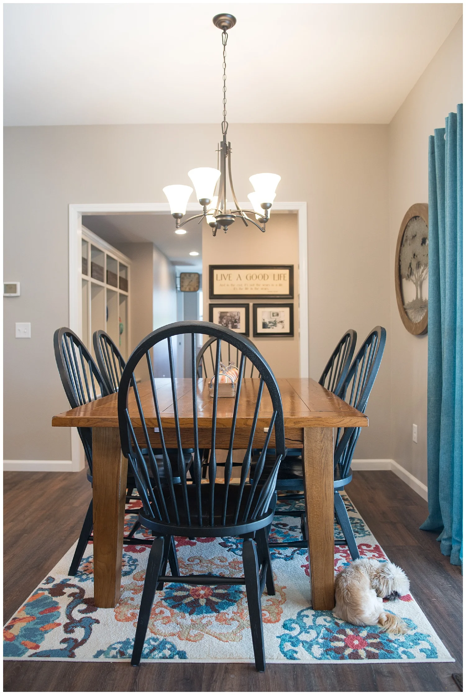 The dining room table came from Uebinger's Furniture. There's little Gus lying on a gorgeous rug and looking out the patio door. She's hung black and white family photos under the Live A Good Life picture. 