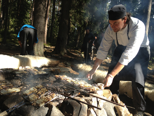 A chef cooks fish and cheese over a campfire.