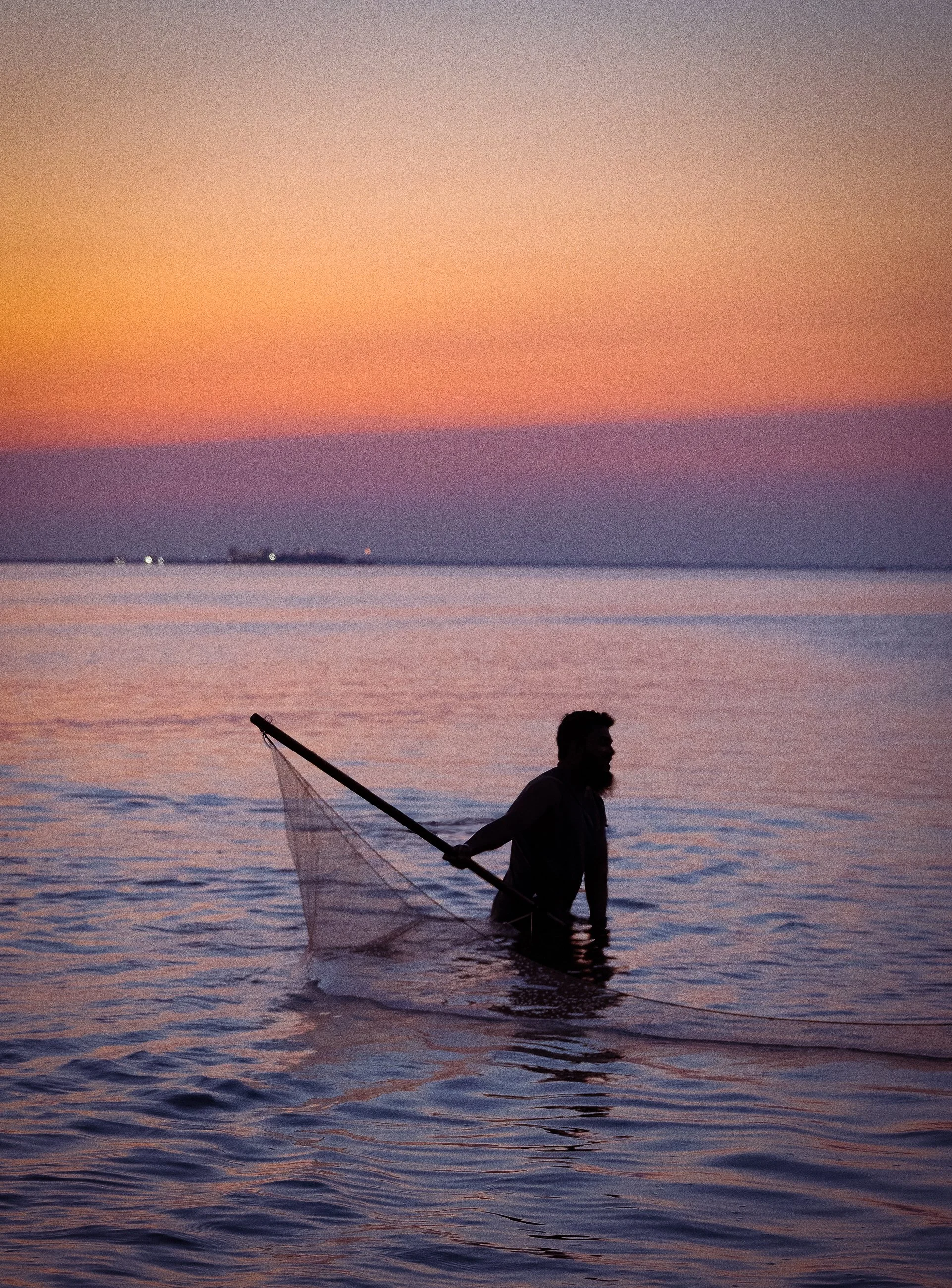 “He Moves Like Memory”
A lone figure pulls the net with quiet resolve. Though separated from the others, he is shaped by their presence — carrying the weight of more than fish or fiber. He holds the memory of everyone who’s ever stood in that water