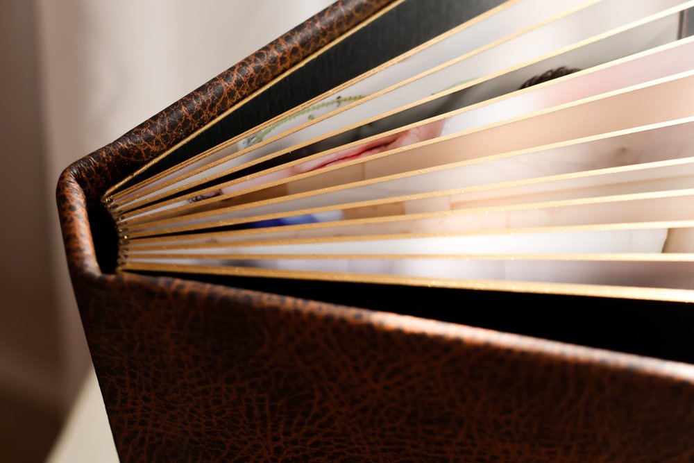 Close-up of a custom photography album with gold gilded pages, antiqued brown leather cover, and additional spreads.