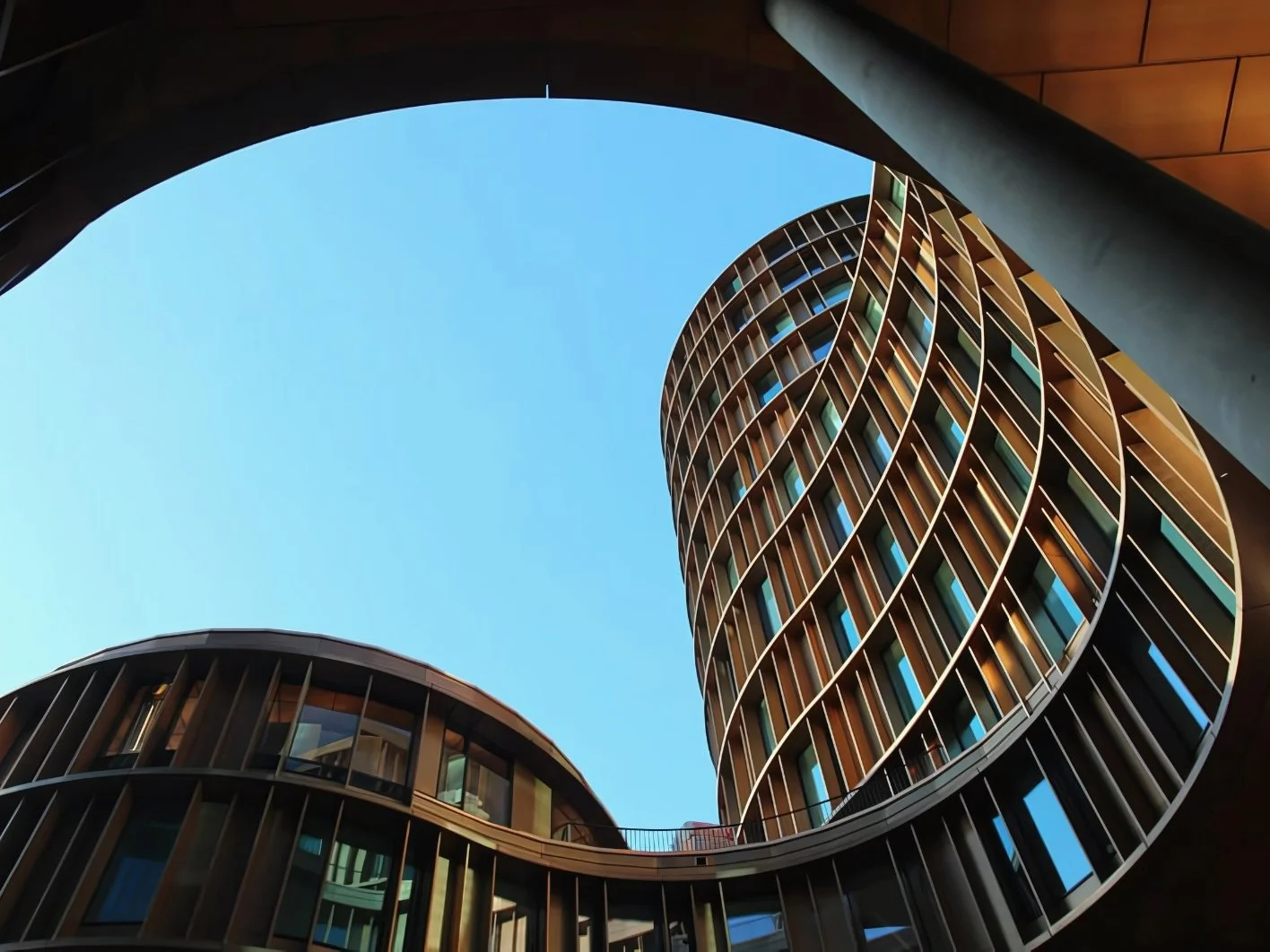 Looking up at the sky through an architectural courtyard with two modern, curved high-rise buildings with glass windows and vertical yellow and dark brown panels, forming a circular shape.