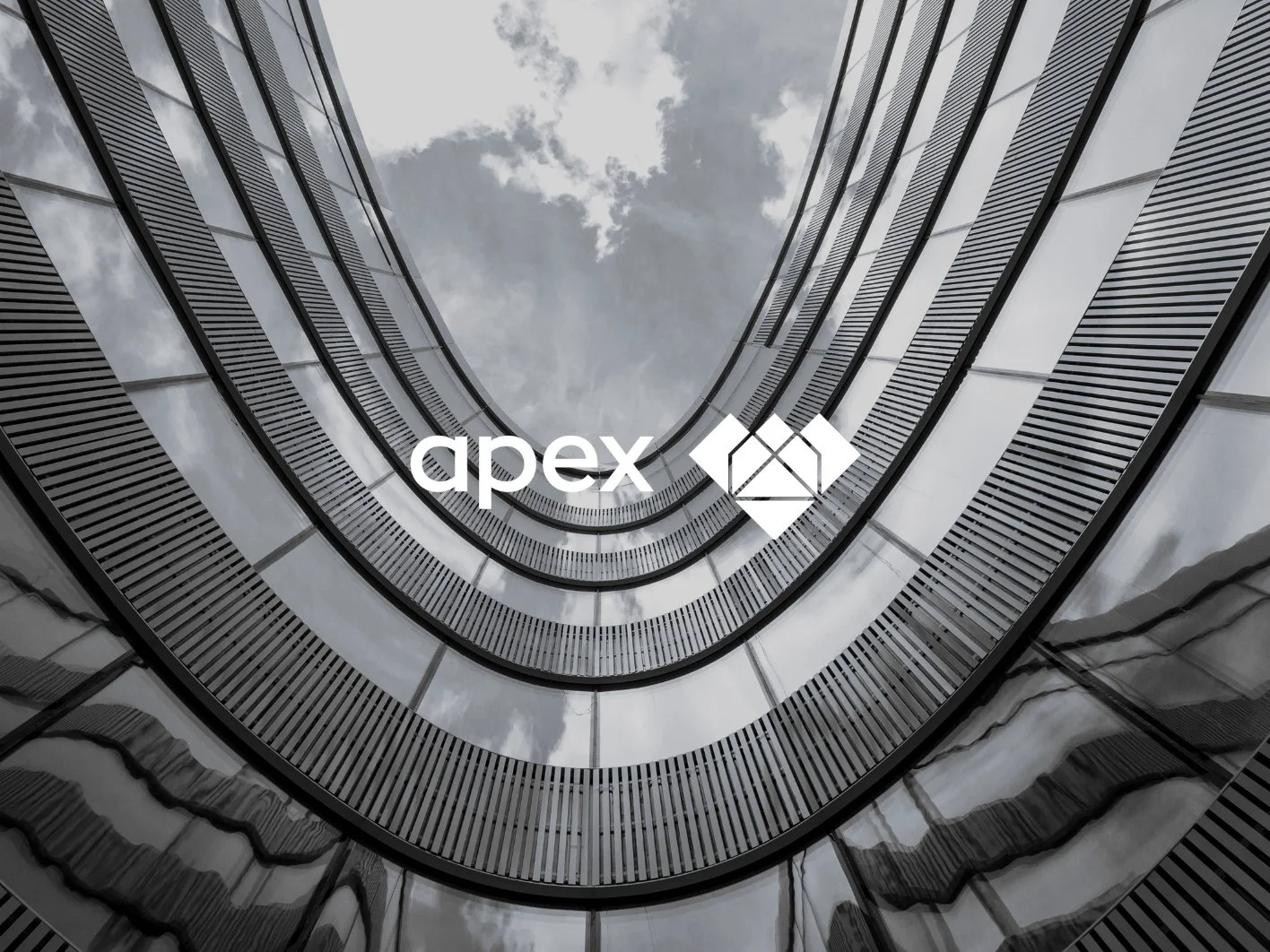 View looking up at a modern, multi-story building with a curved design, glass windows, and metal railings, with a cloudy sky above.