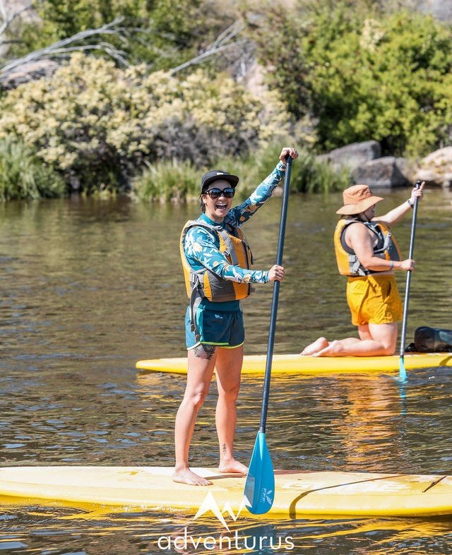 AdventurUs guests paddleboarding on a calm river during a sunny outdoor adventure.