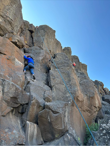 Rock climbers on a cliff face during an outdoor climbing experience organized by AdventurUs.