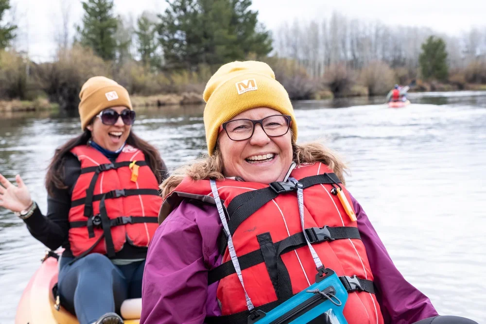 Two women in winter hats and warm jackets smiling together, during a trip organized by AdventurUs.