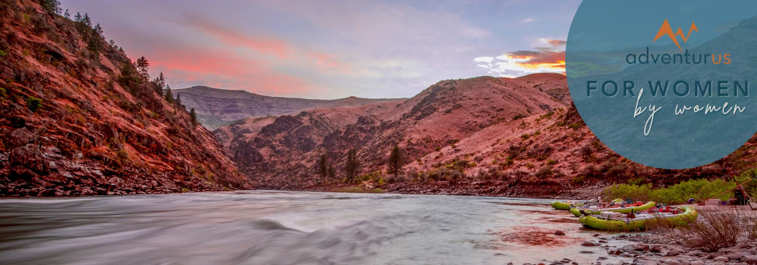 Sunset over a river canyon with rafting boats on the shore and AdventurUs for women by women logo overlay.