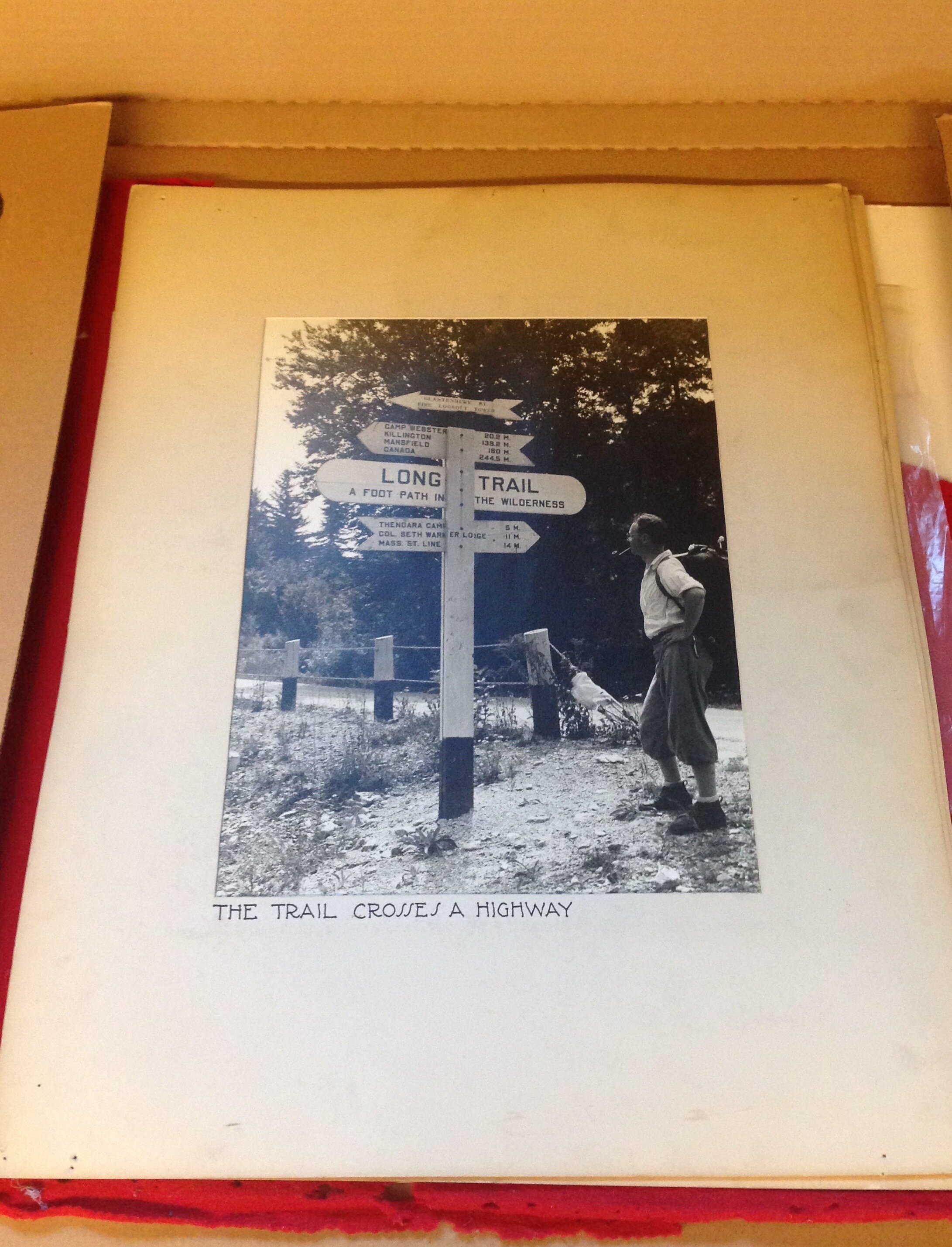   Photographic print of a hiker nearby a Long Trail sign. The caption reads “The Trail Crosses a Highway” (Green Mountain Club Archives).  