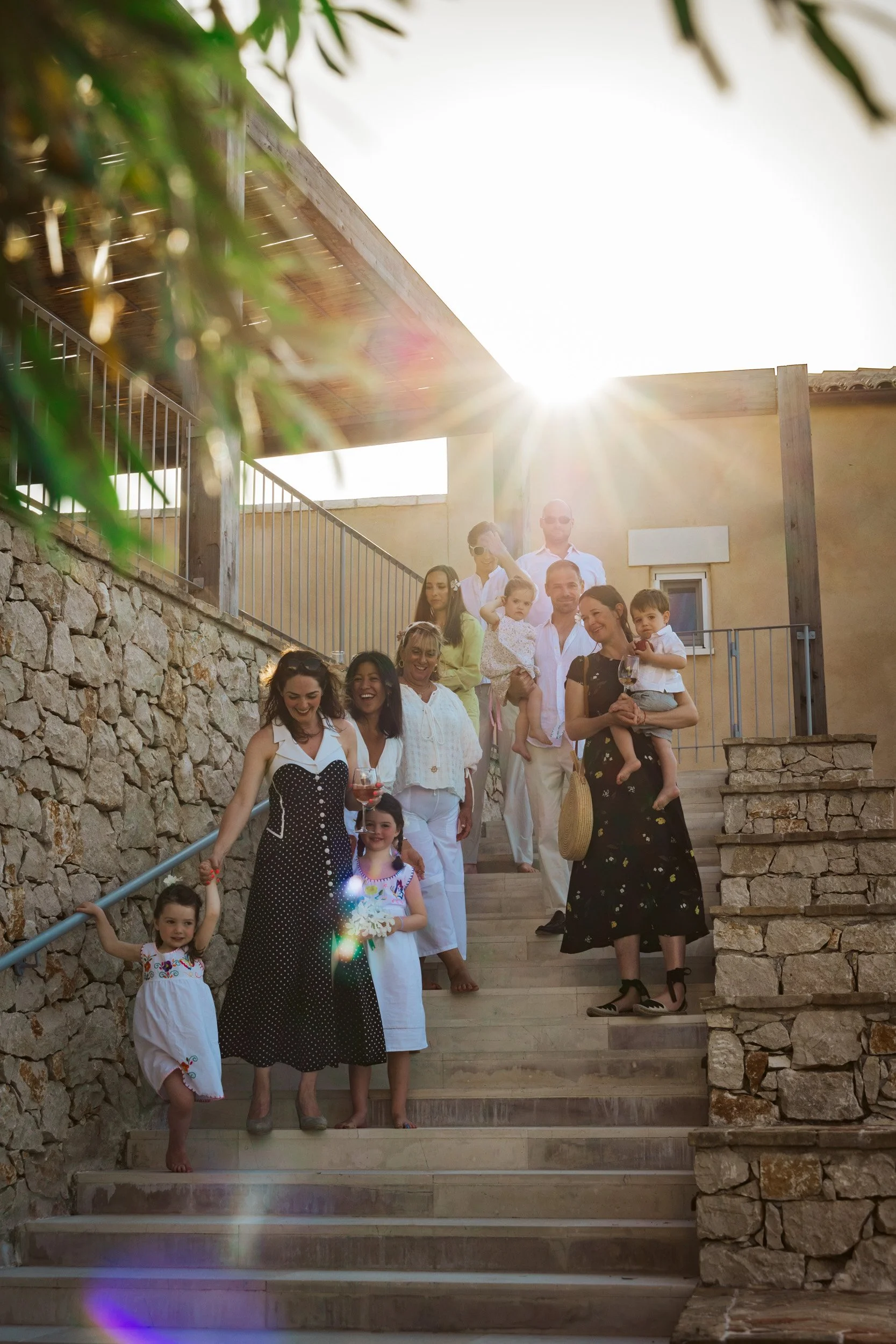 Group of people, including children and adults, standing on outdoor stone stairs during sunset, smiling and enjoying each other's company.