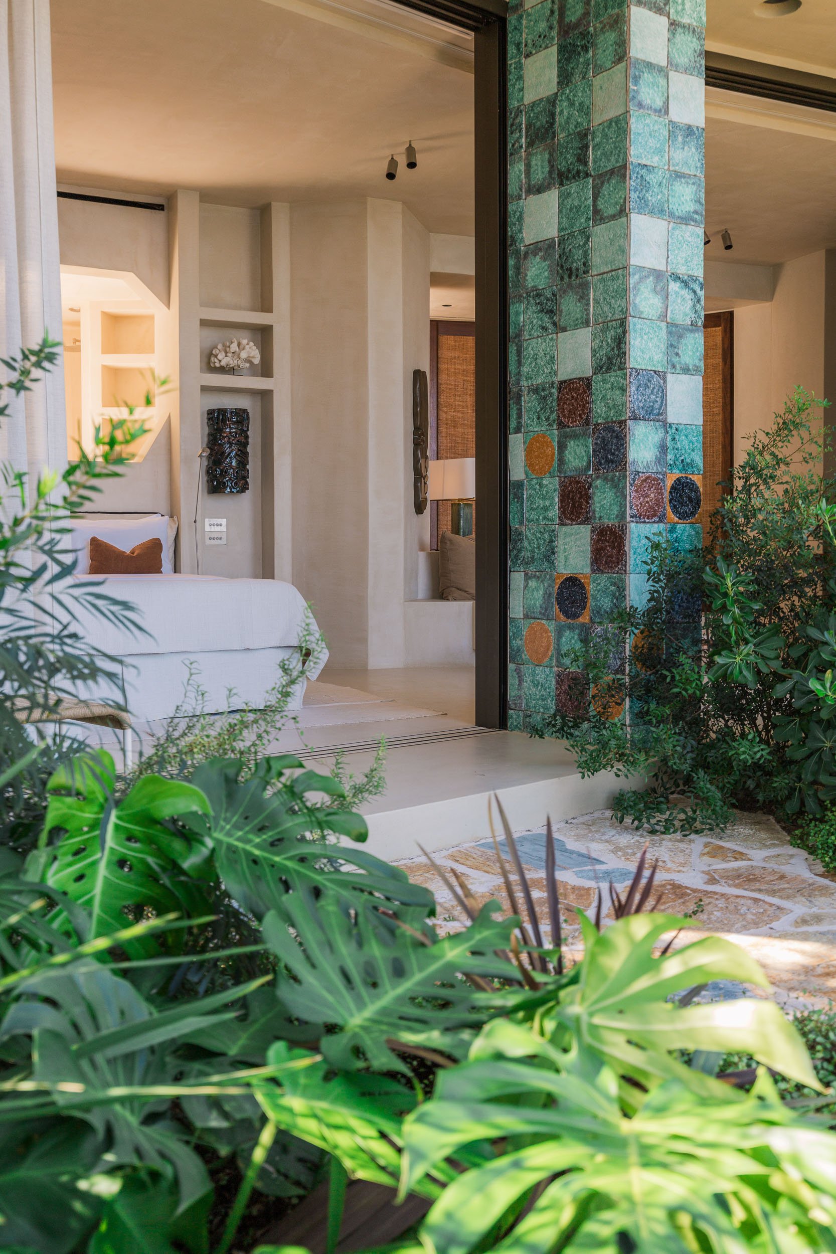 Open sliding glass door revealing a modern living space with white walls, decorative wall art, and lush green plants outside.