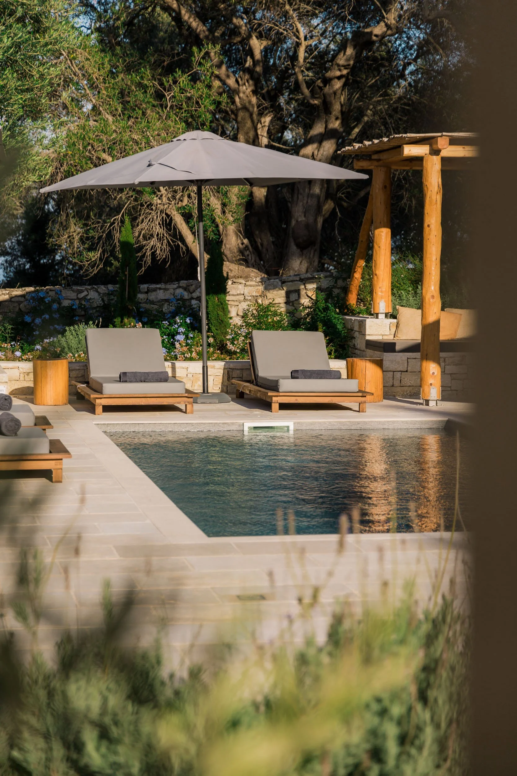 Poolside area with two lounge chairs, an umbrella, and a pergola in a landscaped backyard.