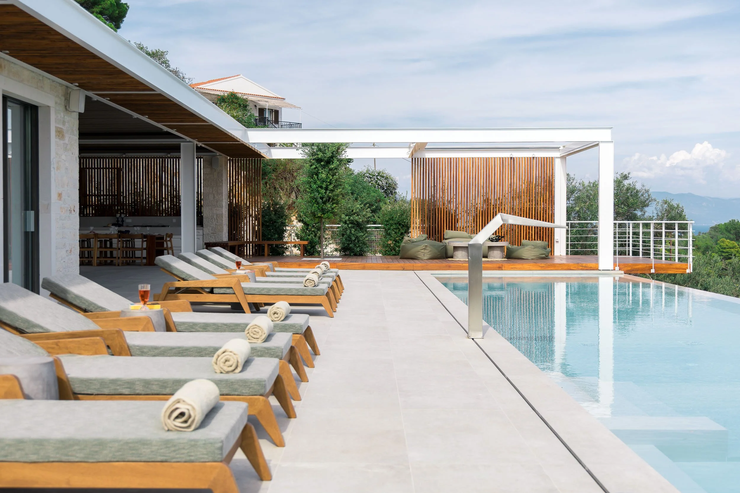 Luxury outdoor pool area with lounge chairs, towels, and drinks, overlooking a scenic landscape with trees and mountains.