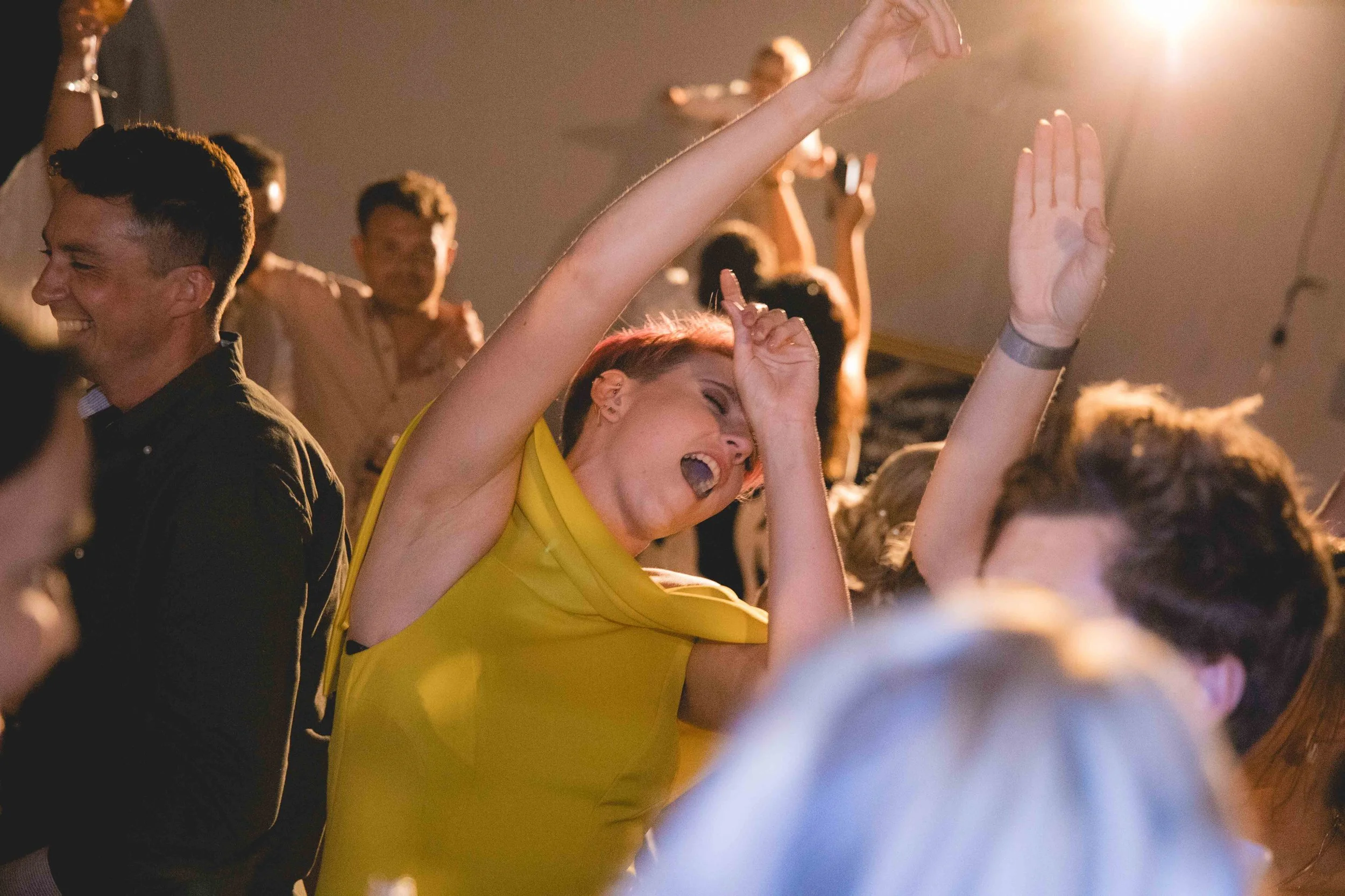 People dancing and enjoying a lively party or concert under warm lighting, with some raising their hands.