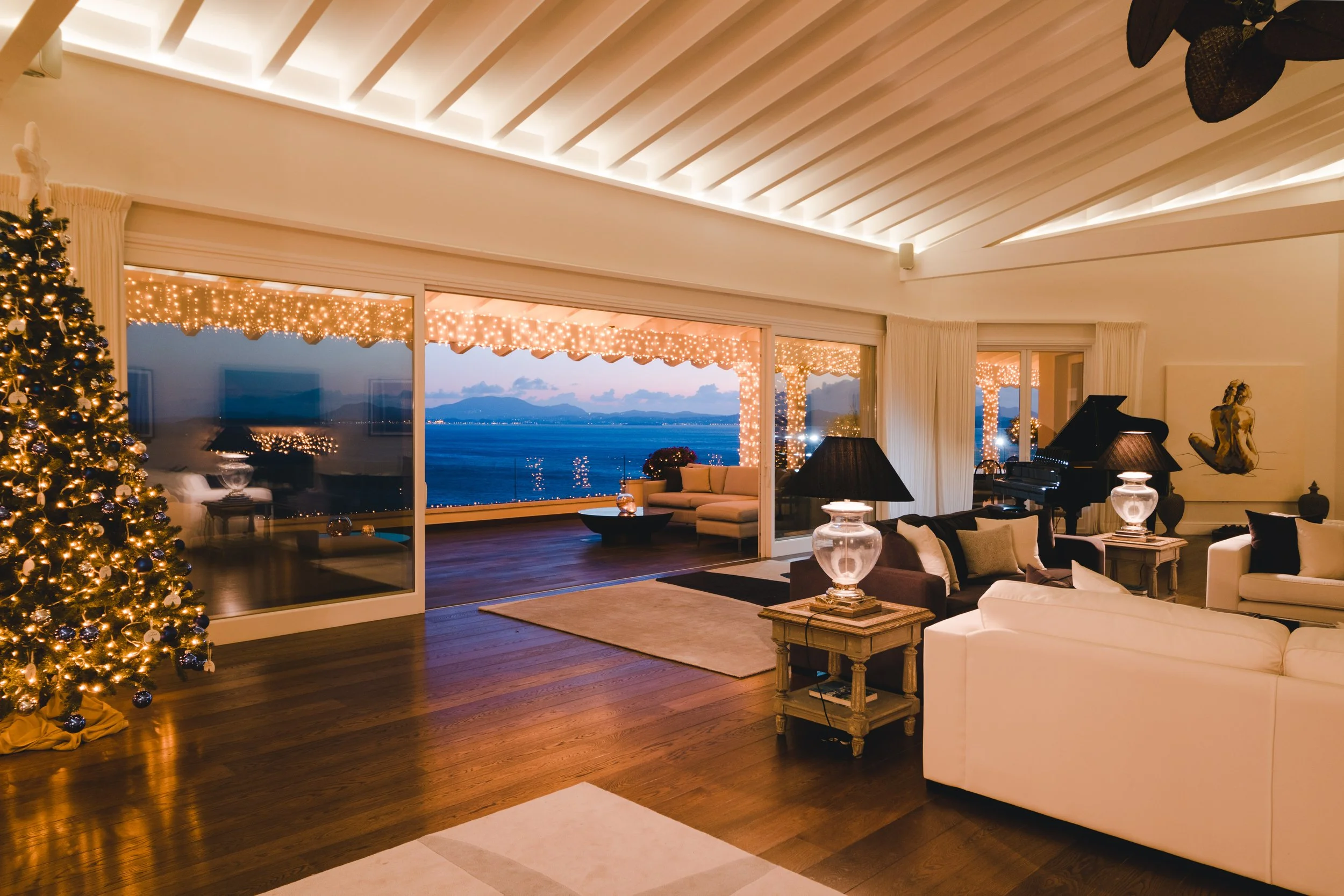 Living room decorated for Christmas with a Christmas tree, Christmas lights, and a view of the ocean through large sliding glass doors.