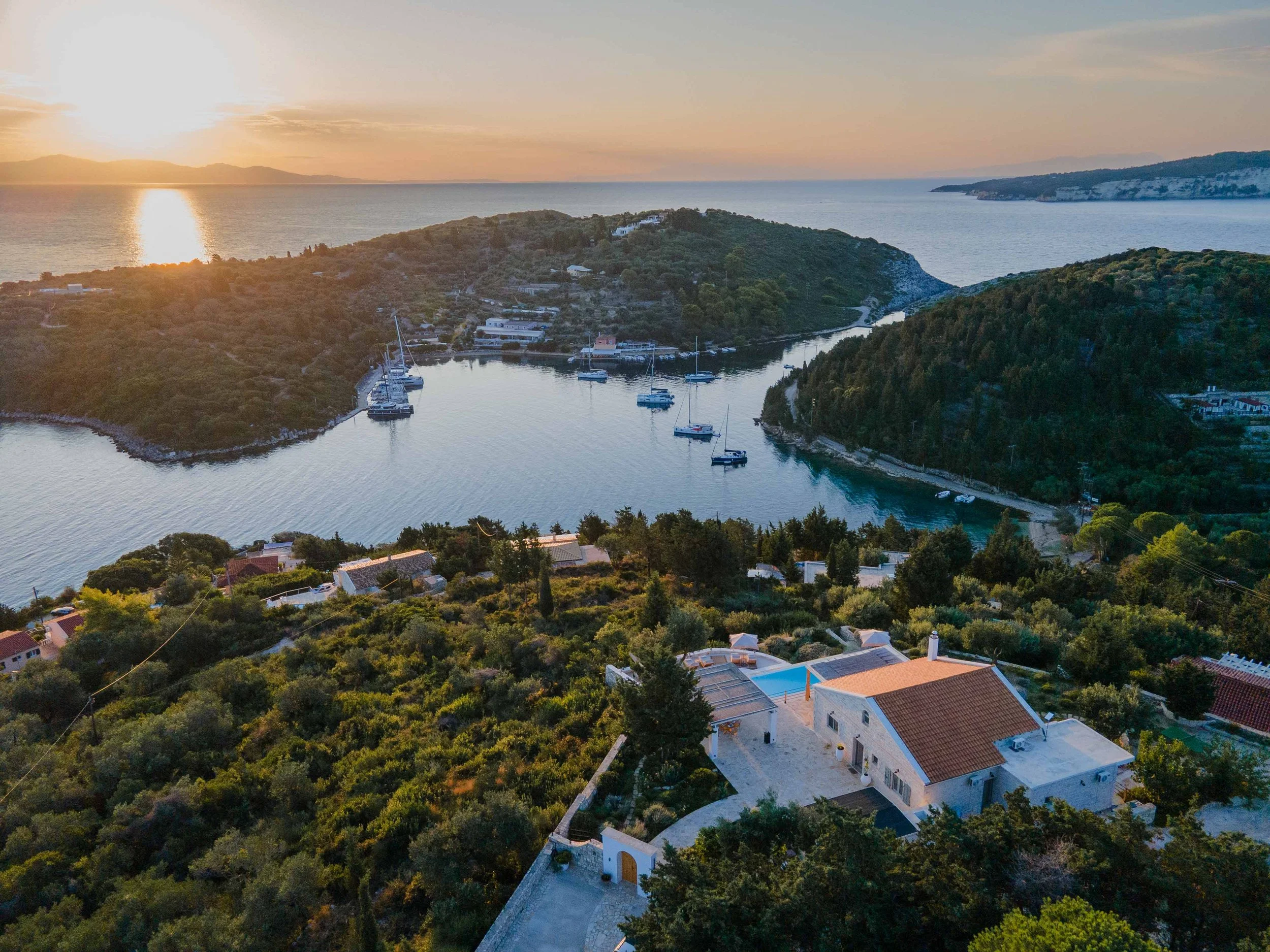Sunset over a coastal bay with boats anchored near green islands and houses surrounded by trees