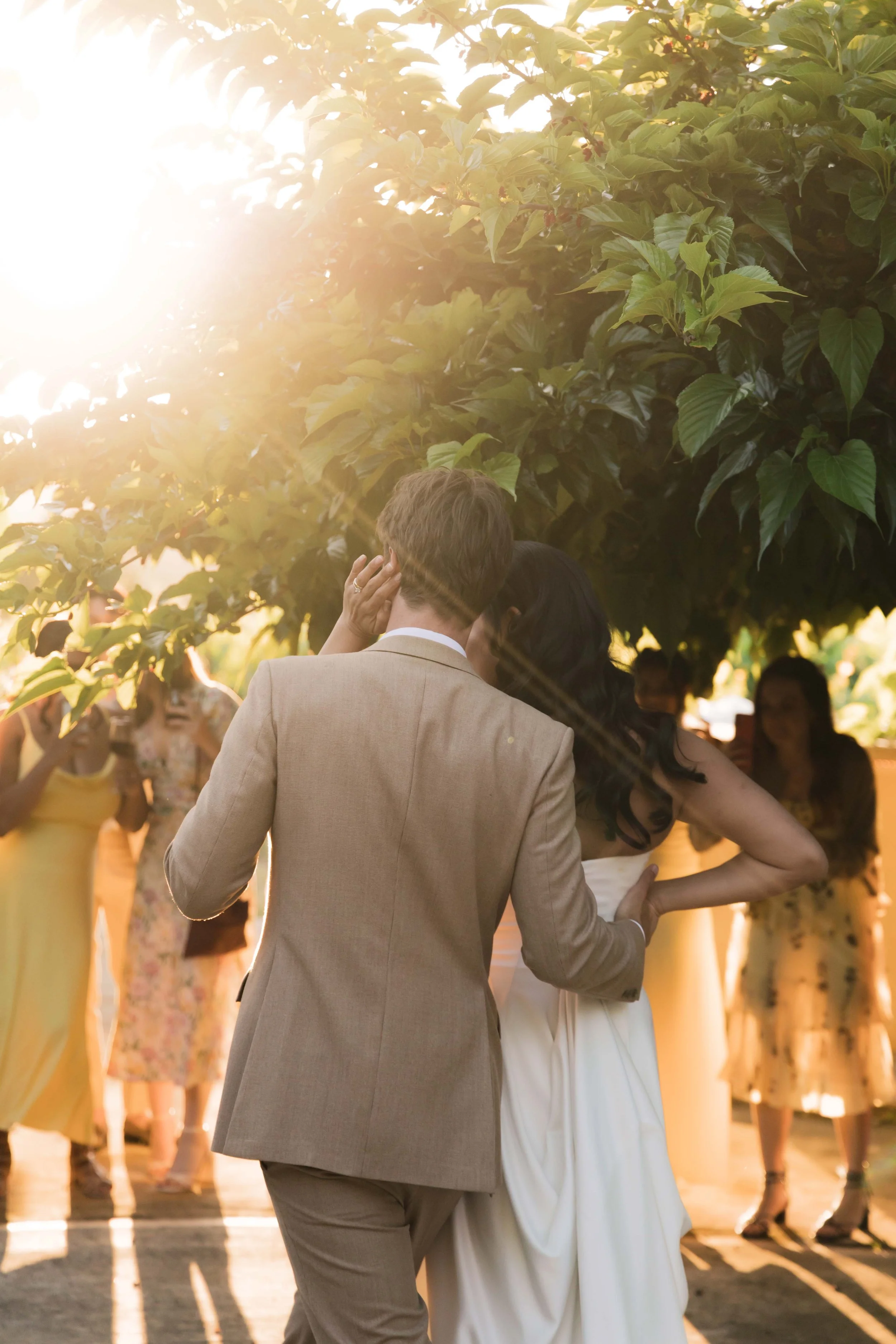Couple dancing outdoors at their wedding reception during sunset, surrounded by guests.
