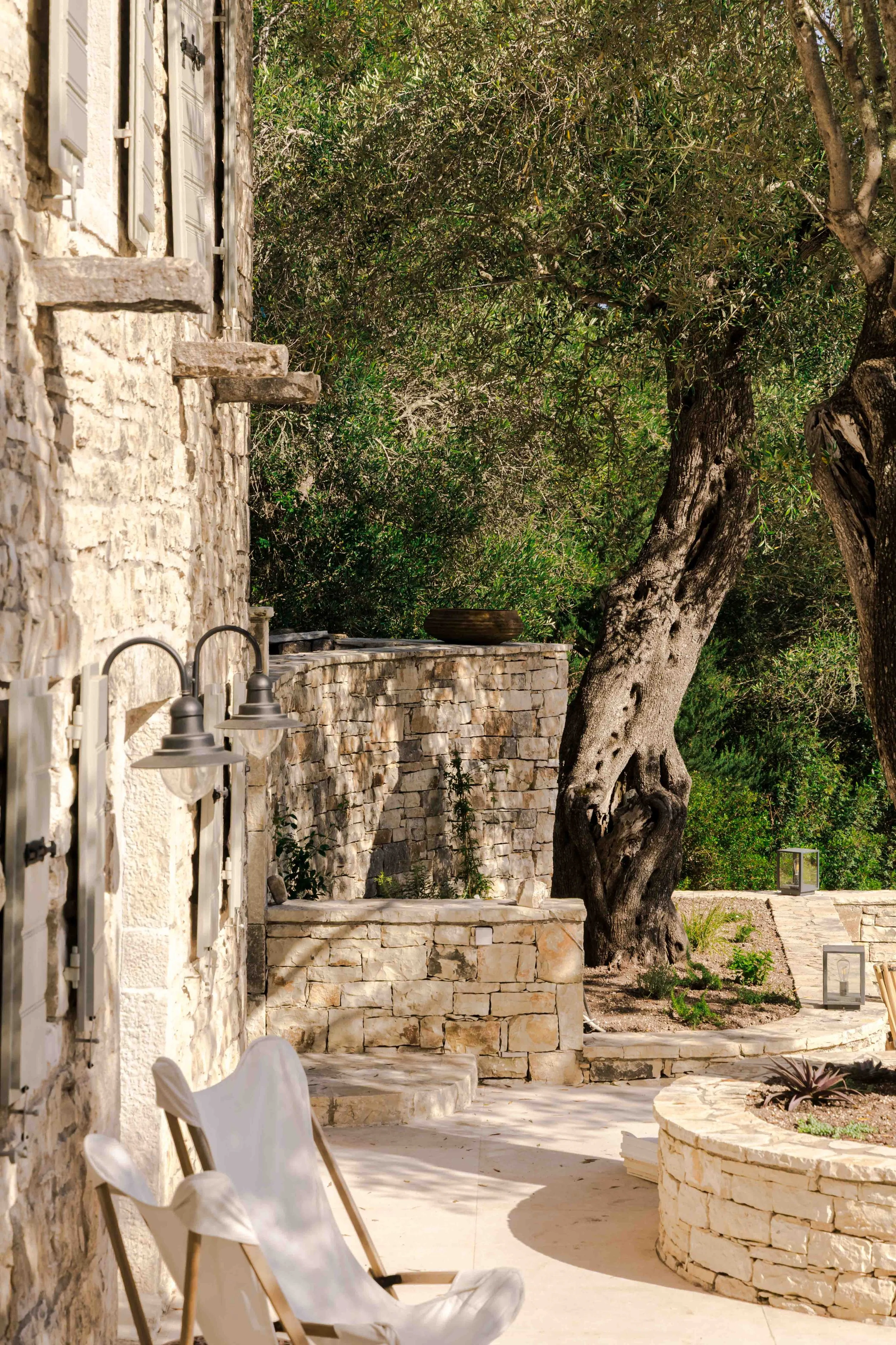 Stone house with outdoor patio, surrounded by trees, with lounge chairs in the foreground.