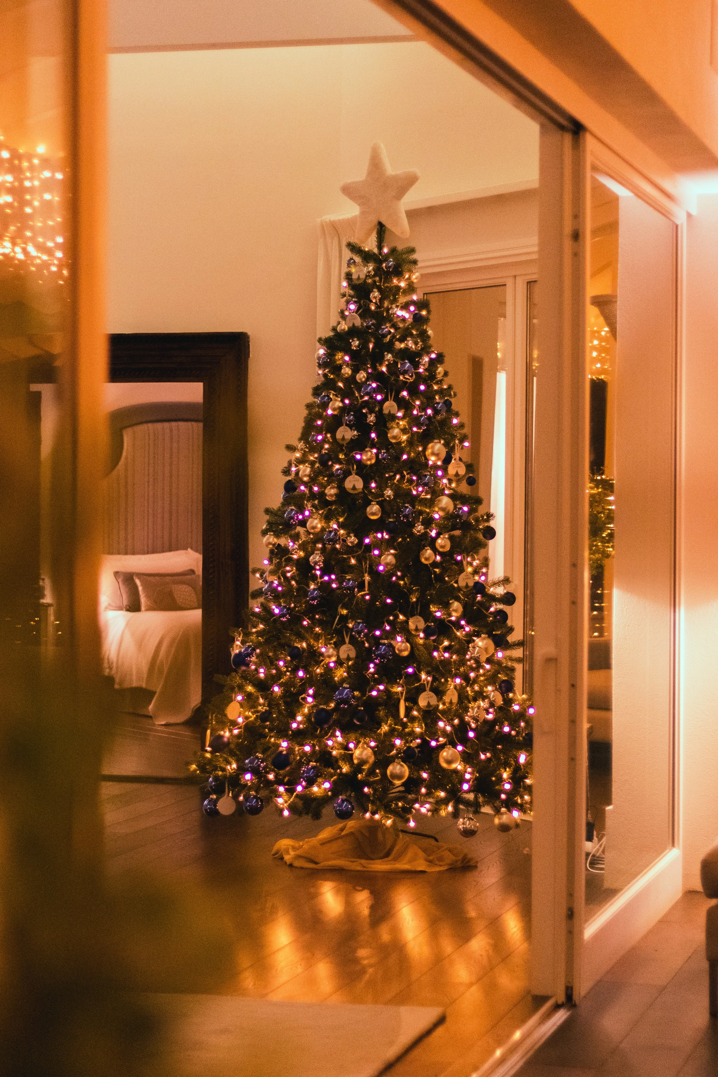 A decorated Christmas tree with ornaments and purple lights, topped with a star, in a cozy room.