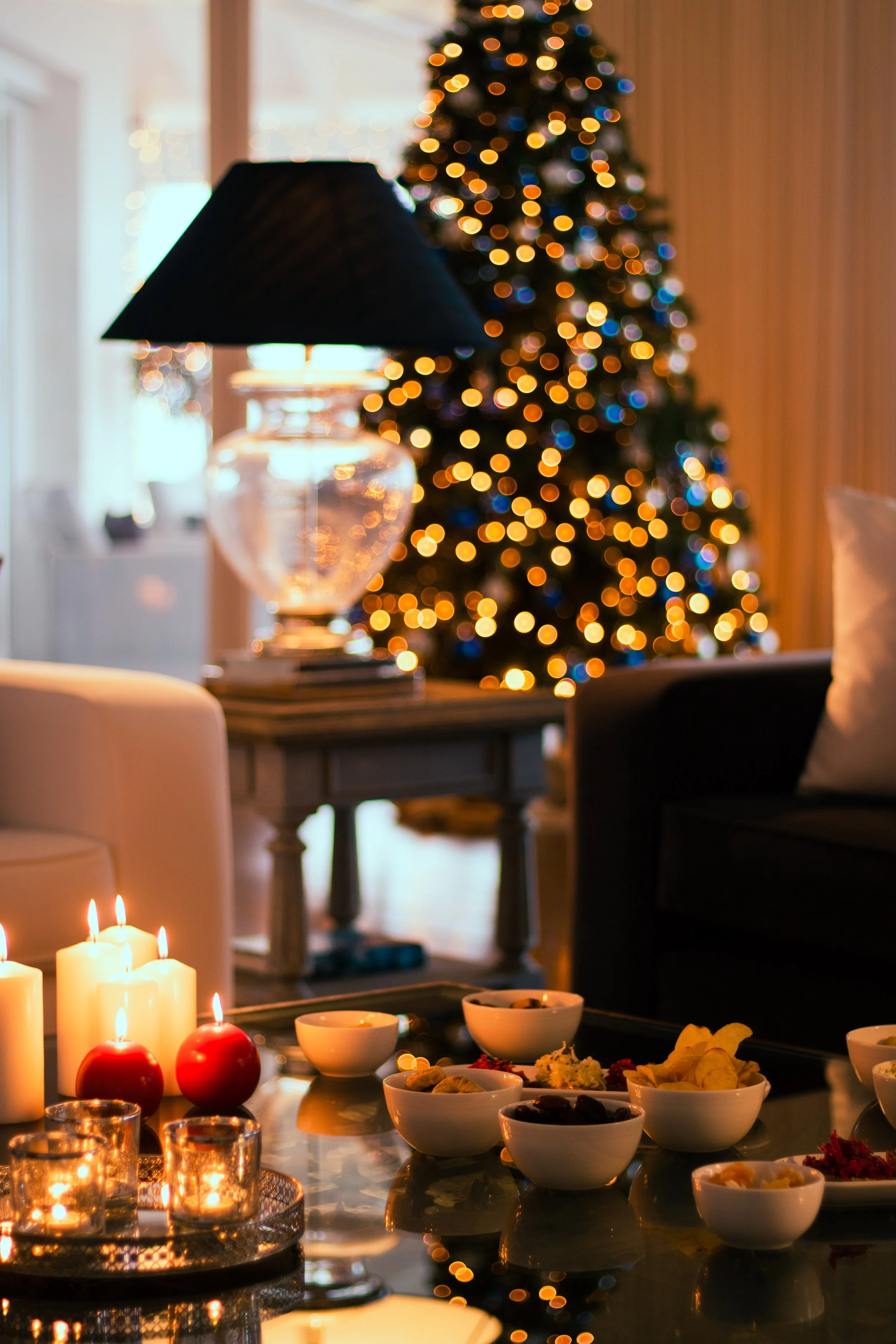 A cozy living room decorated for Christmas with a lit Christmas tree, candles, and snacks on a table.