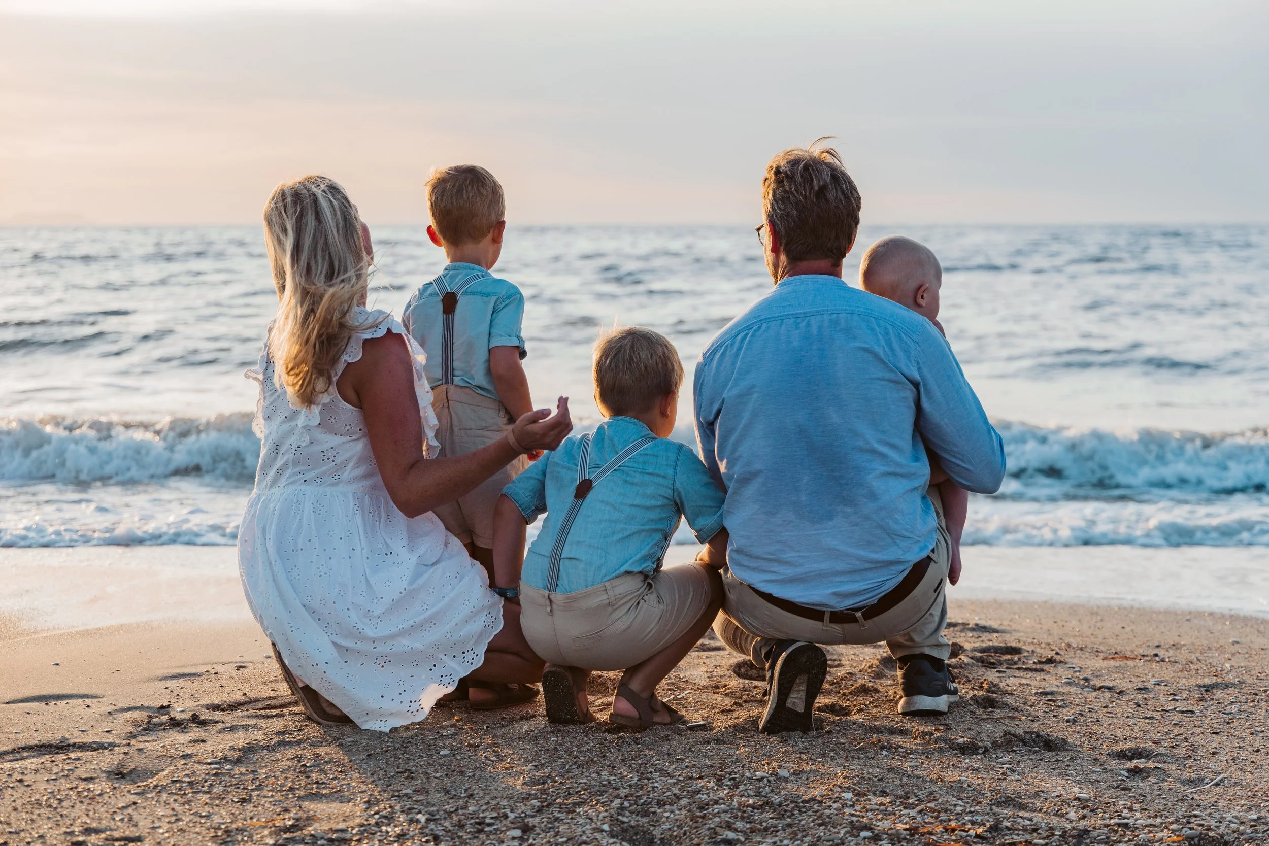 Family sitting on the sandy beach during sunset, looking out at the ocean waves.