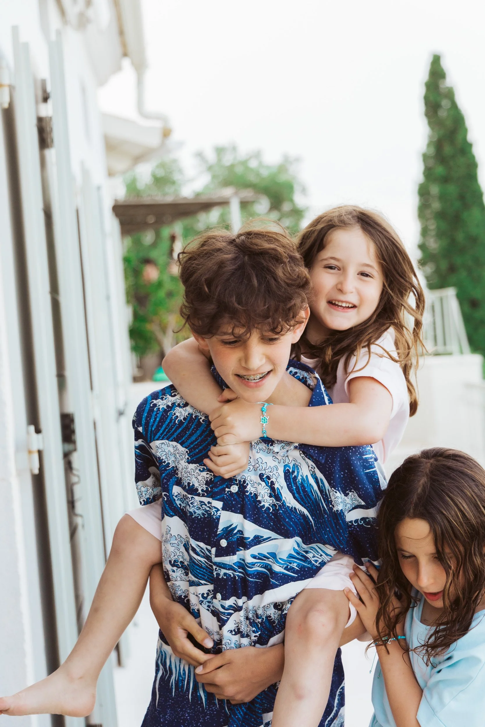 Children playing outside, with one boy giving a piggyback ride to a girl and another girl nearby, all smiling and having fun.