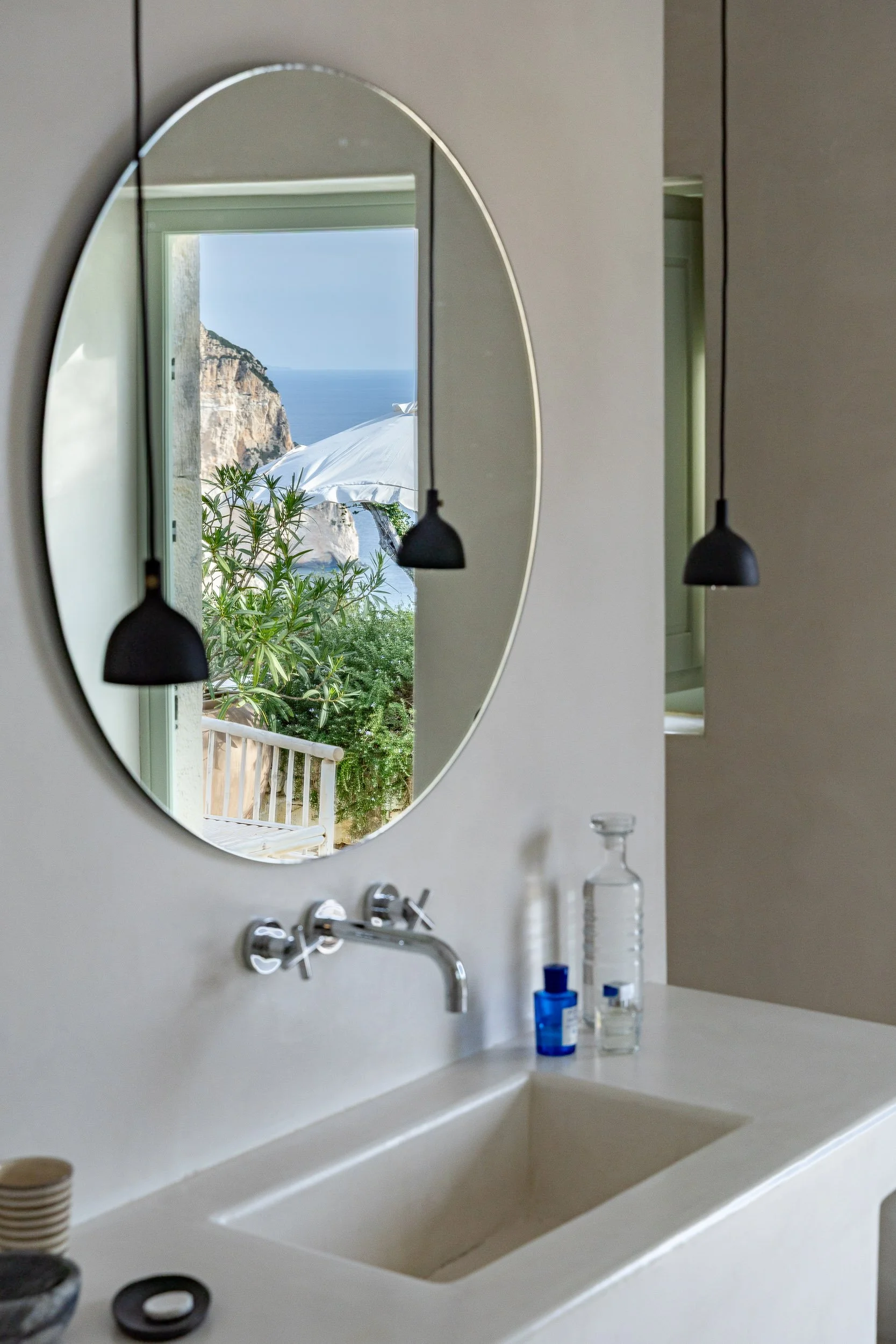 Bathroom sink with mirror reflecting an outdoor scene of beach, cliffs, green plants, and a white umbrella.