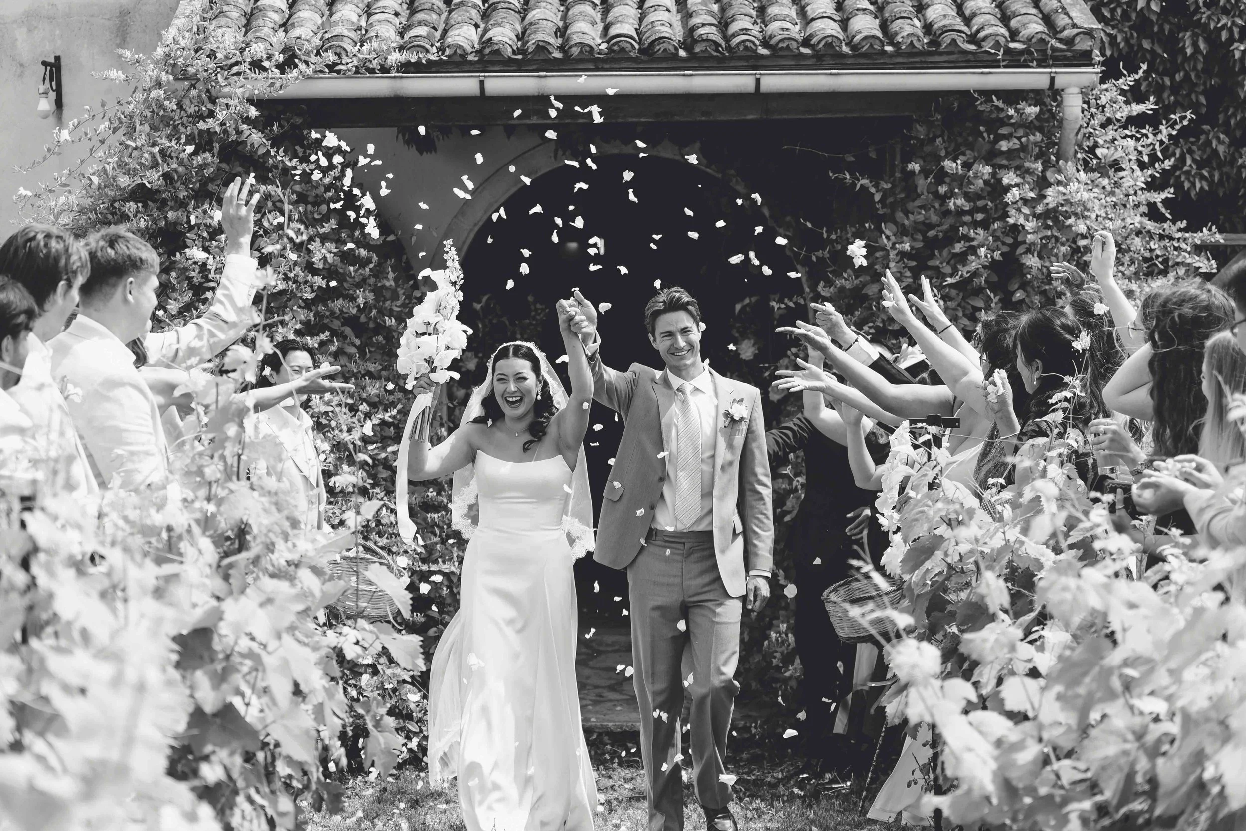 A bride and groom walking through confetti after their wedding ceremony, surrounded by friends and family.