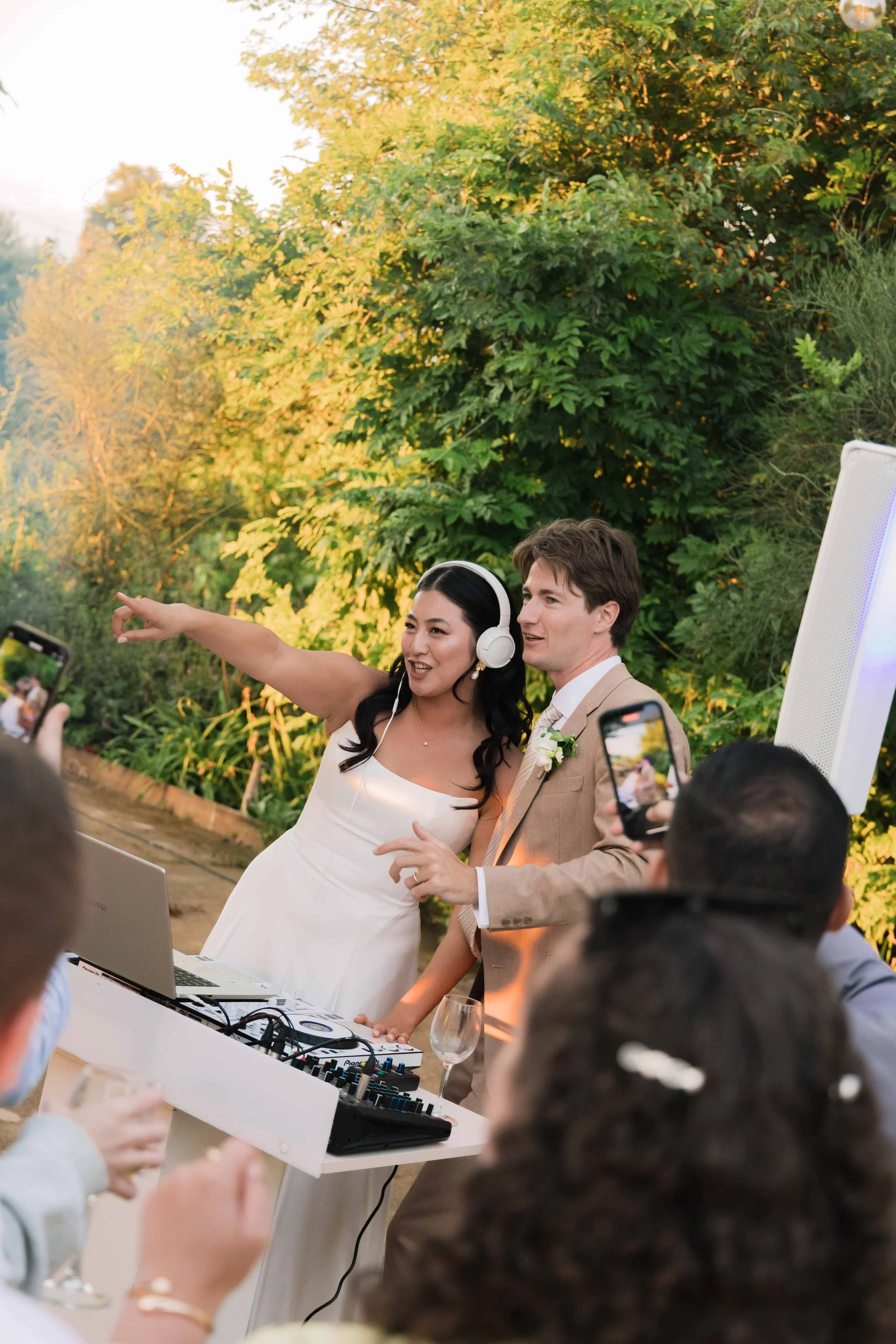 A bride and groom dancing and celebrating at their wedding reception outdoors, with guests taking photos and videos.