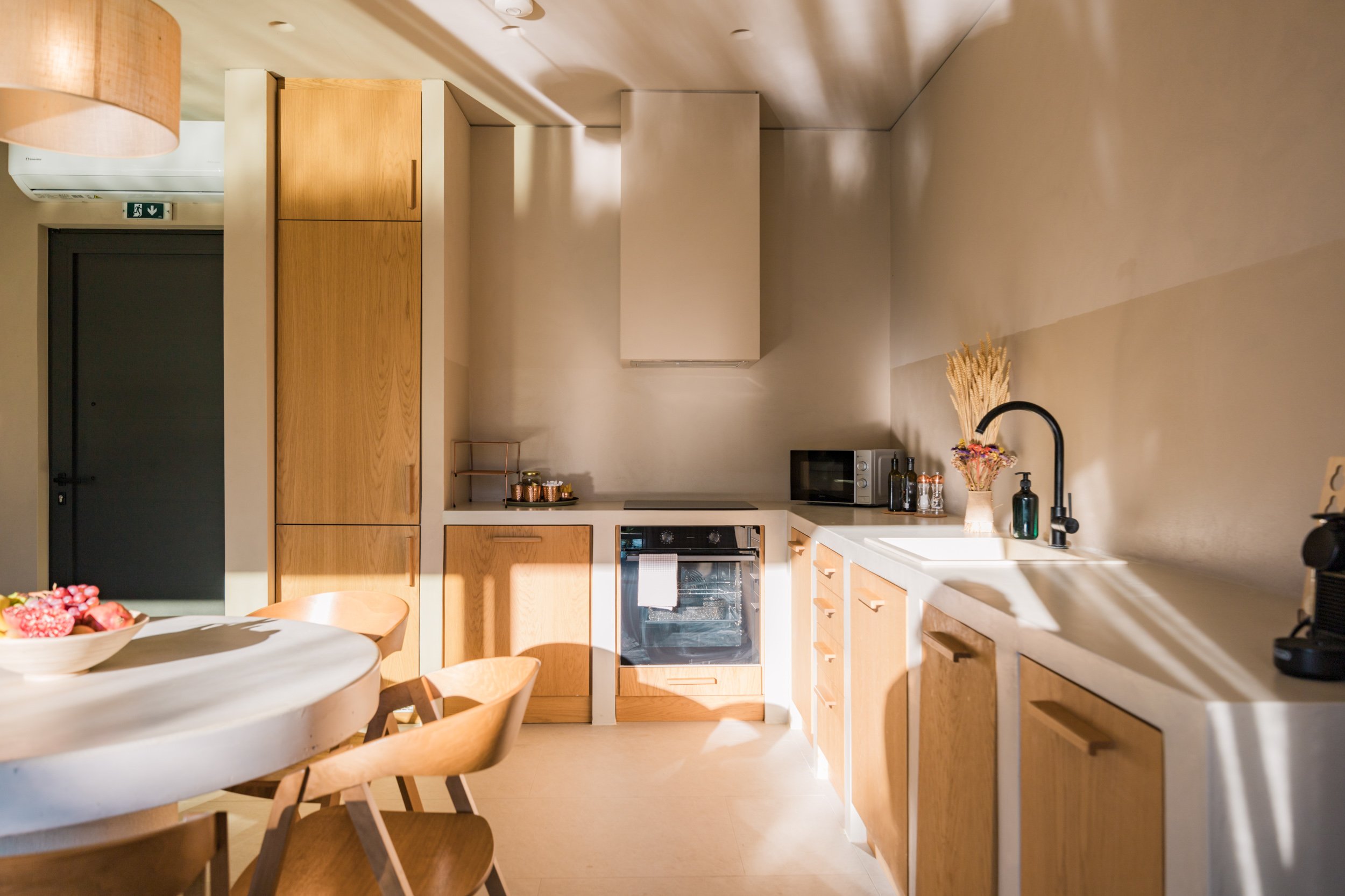 A modern kitchen with wooden cabinets, a white countertop, a built-in oven, a microwave, a black faucet, and natural light streaming in.