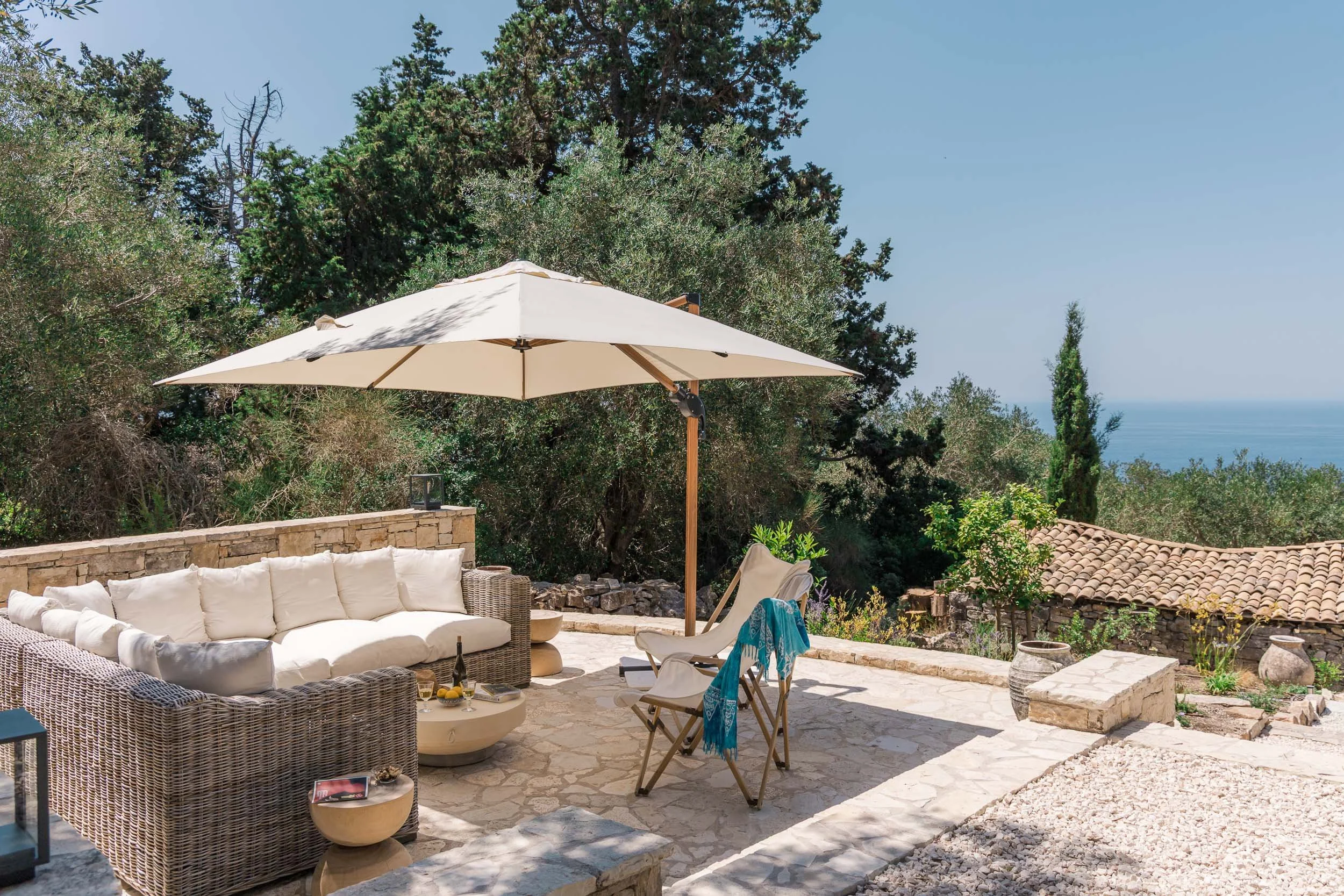 Outdoor patio with wicker sofa, chairs, and umbrella overlooking a scenic landscape of trees and the ocean in the distance.