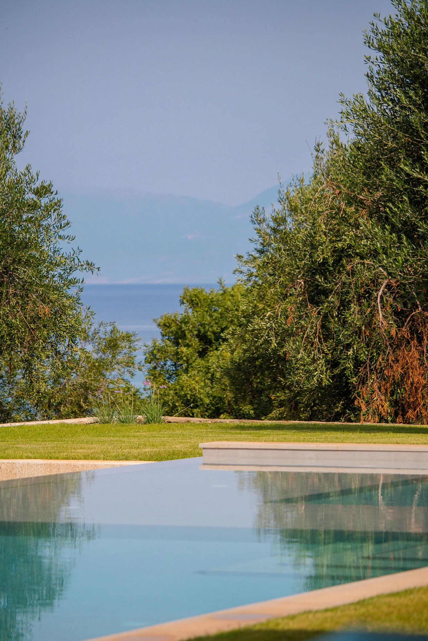 A swimming pool with a view of trees, grassy area, and mountains in the distance.