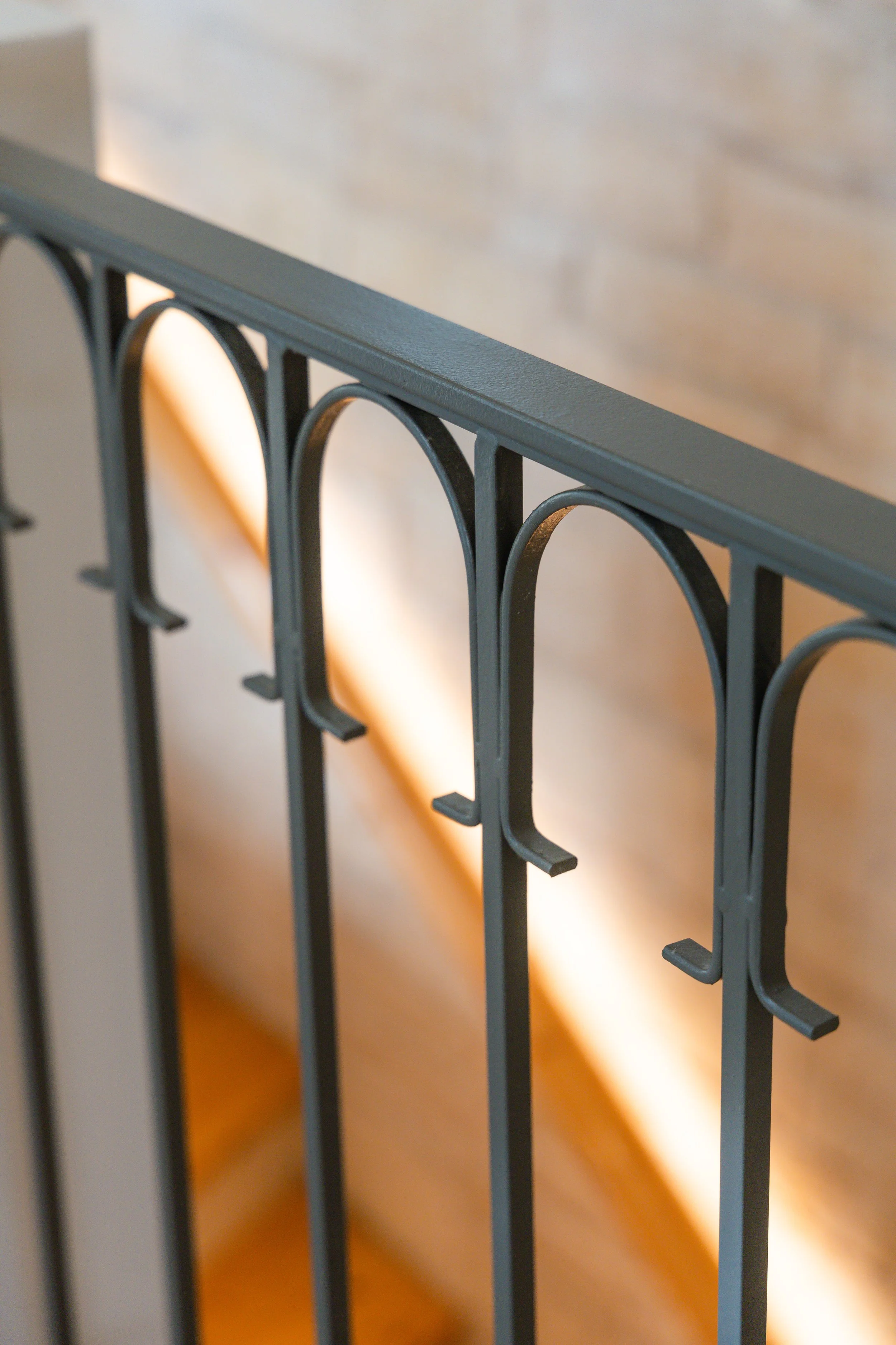 Close-up of a black metal railing with arched details, against a blurred wooden background.