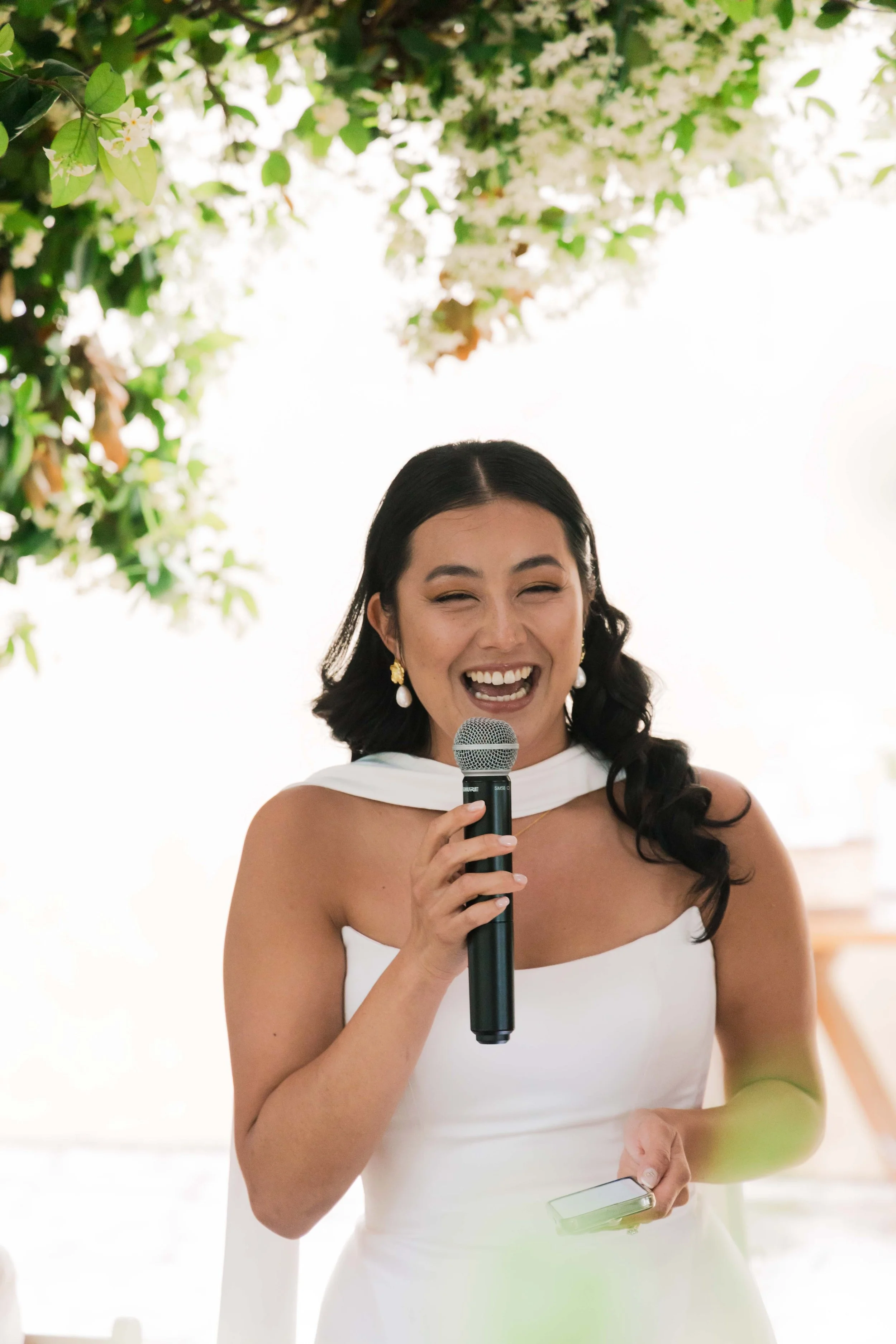 A woman in a white dress holding a microphone and smiling.