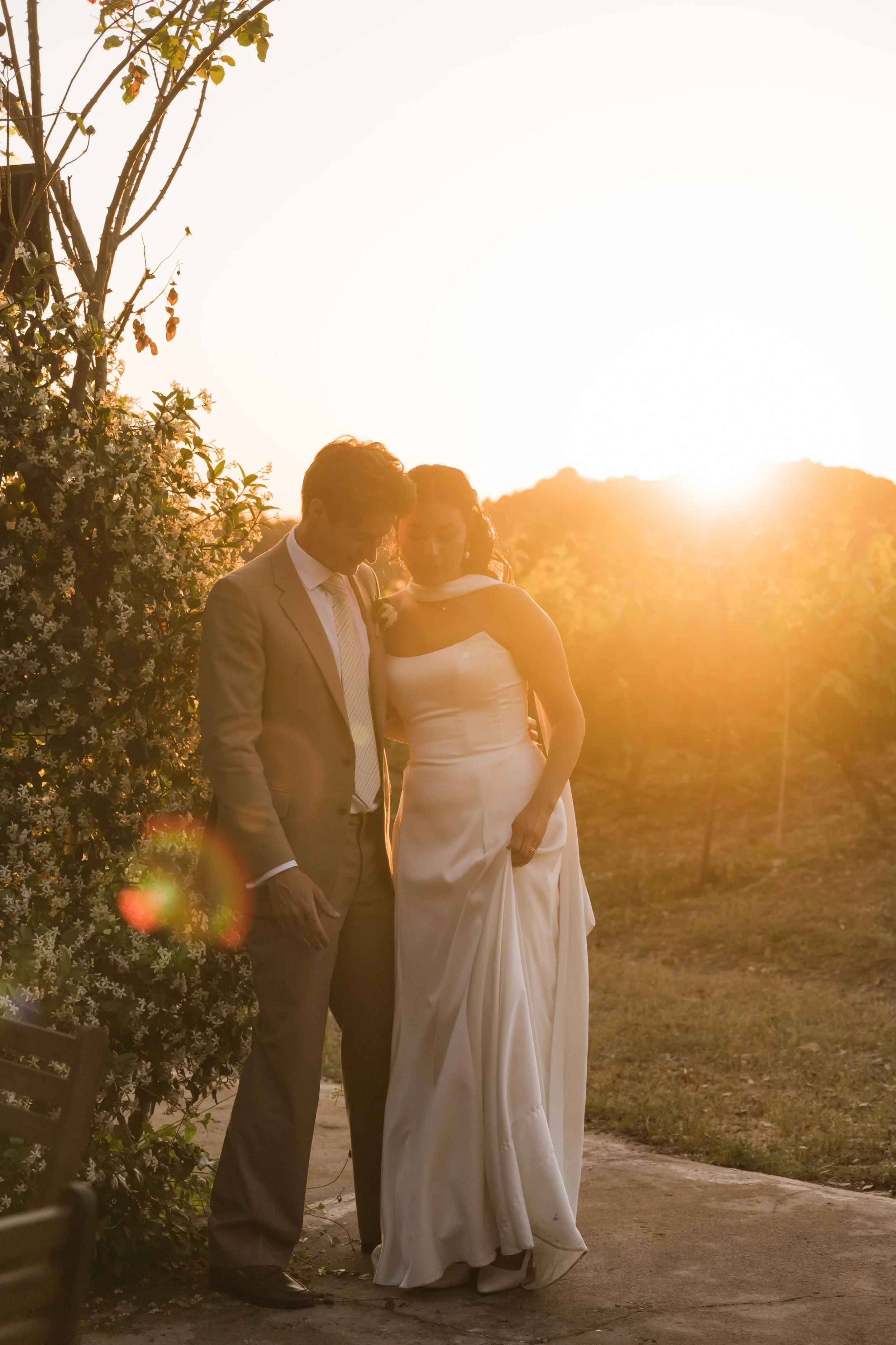A bride and groom standing close together outdoors during sunset.