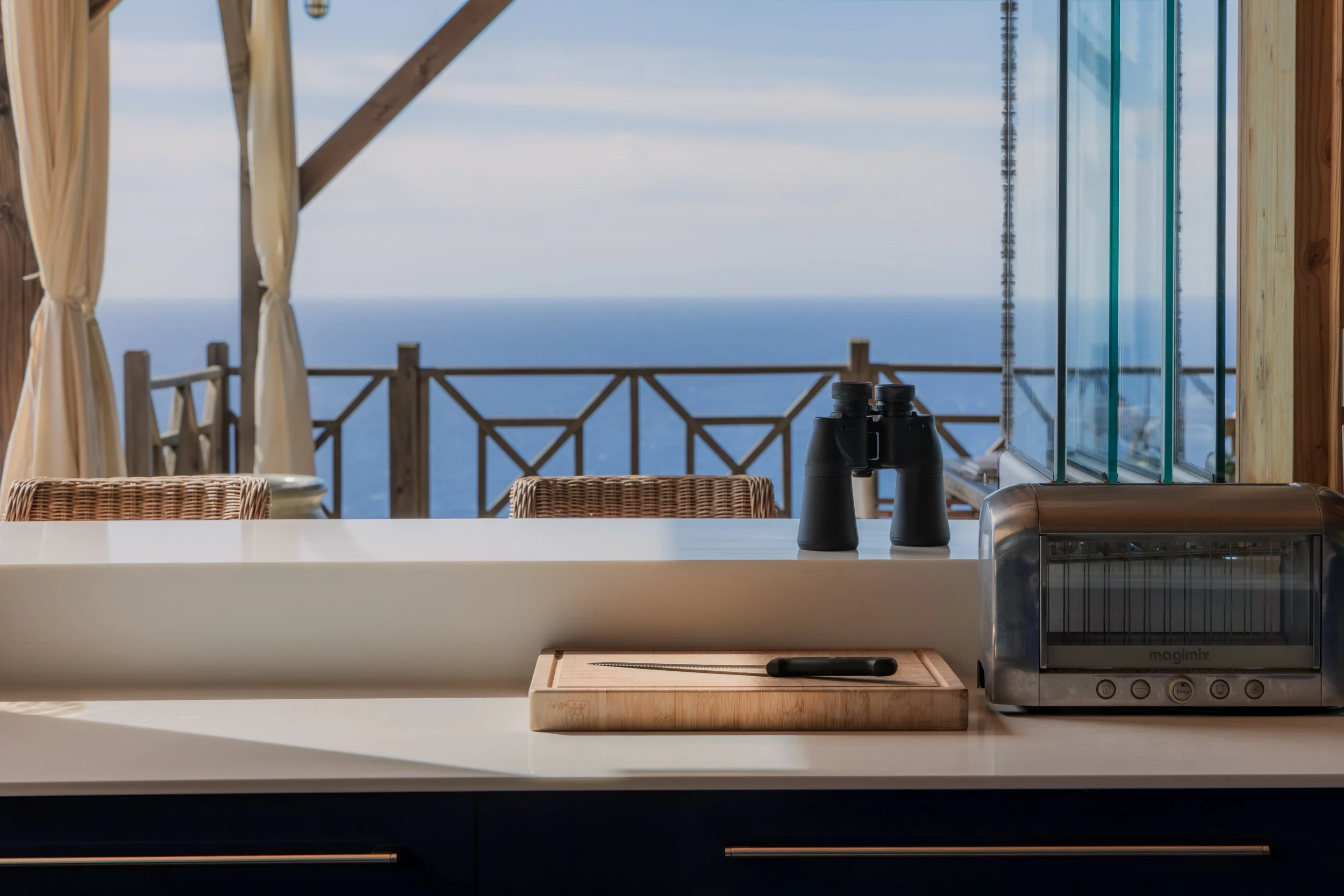 Kitchen counter with binoculars, toaster, and cutting board, overlooking a balcony with ocean view