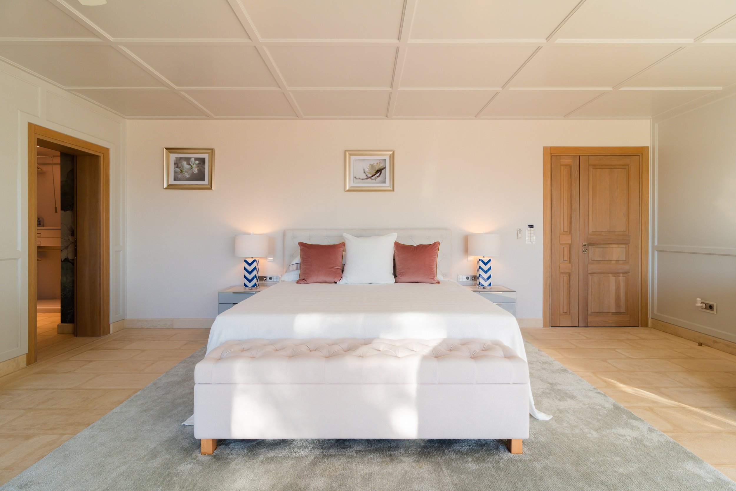 A bedroom with a bed, two nightstands with lamps, and framed artwork on the wall above the bed.