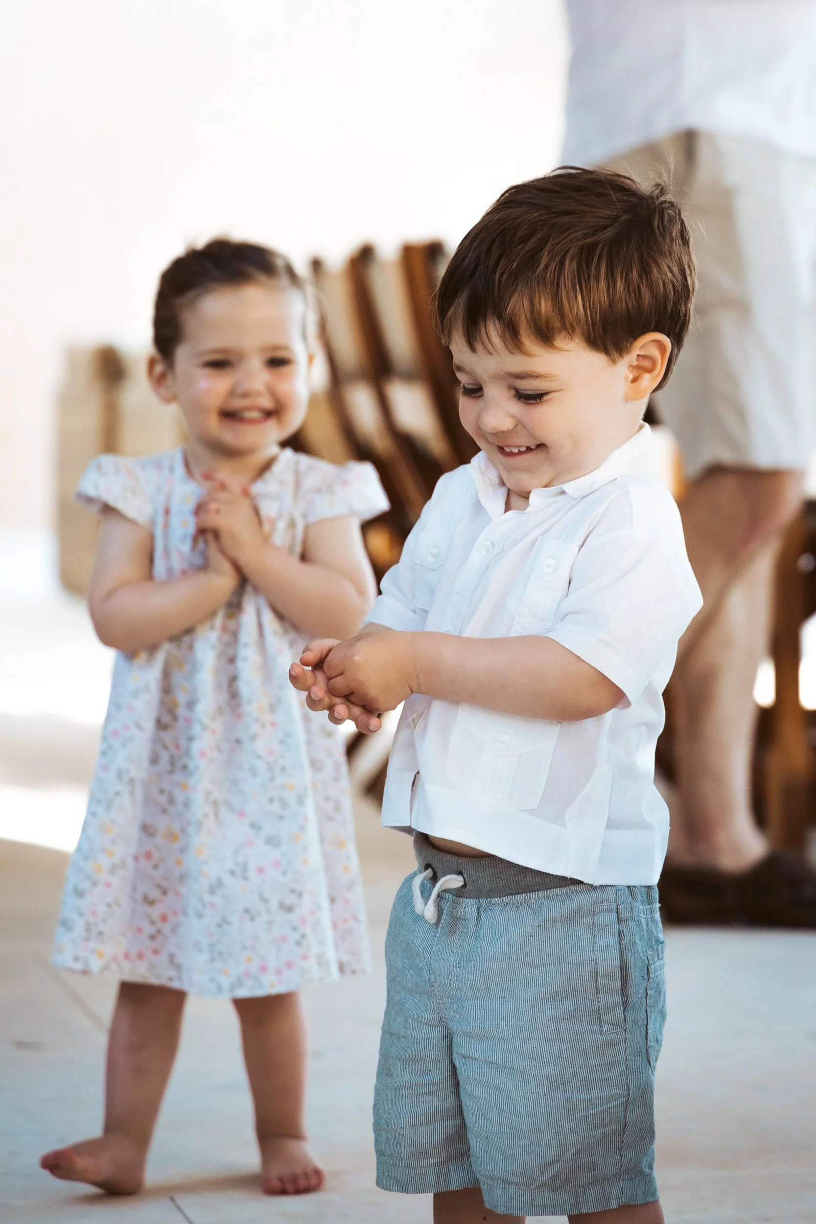 A boy and a girl happily interacting indoors, with the boy showing something on his hands and the girl smiling behind him.