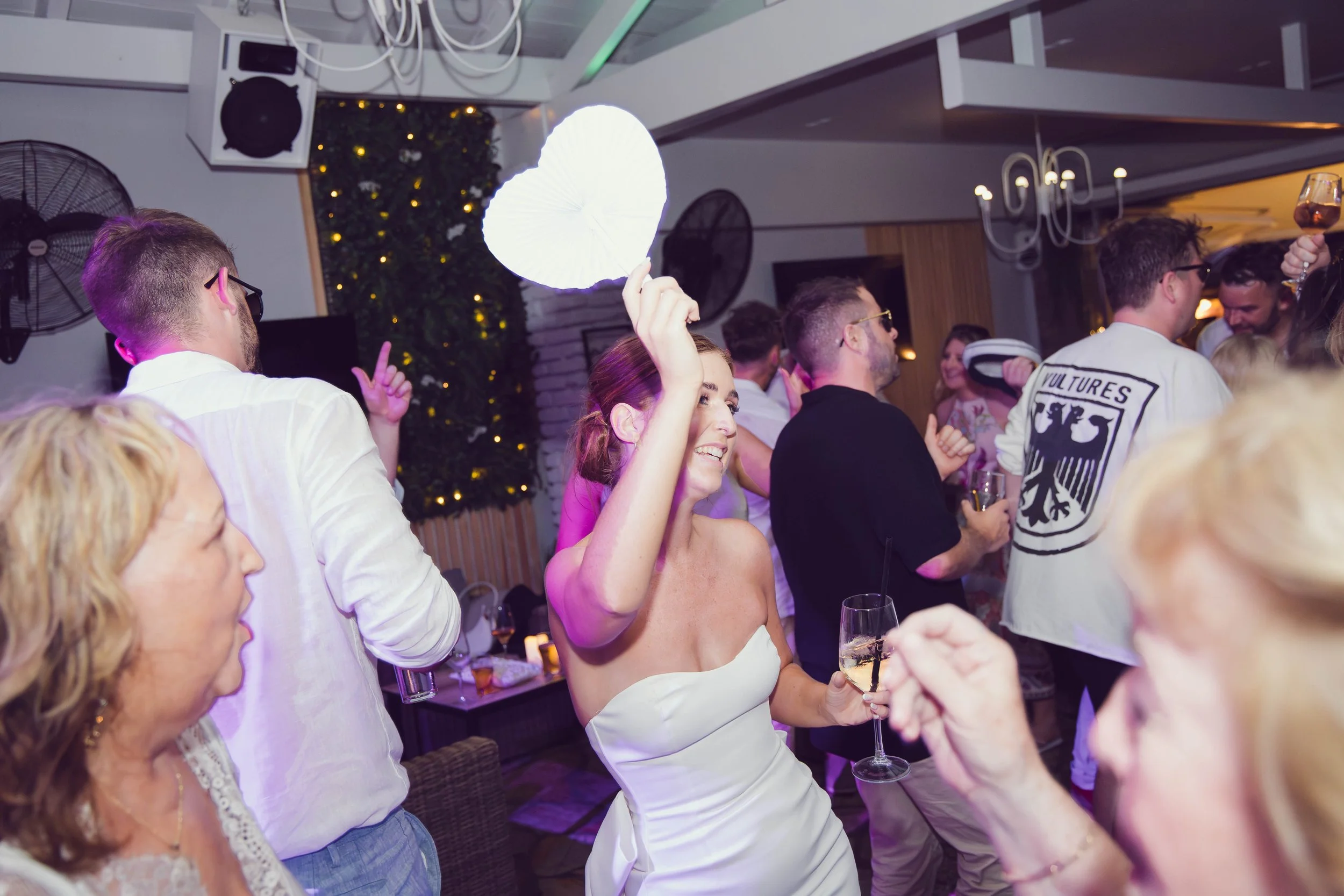 A woman in a white strapless dress dancing and smiling while holding a glass of champagne at a party or celebration