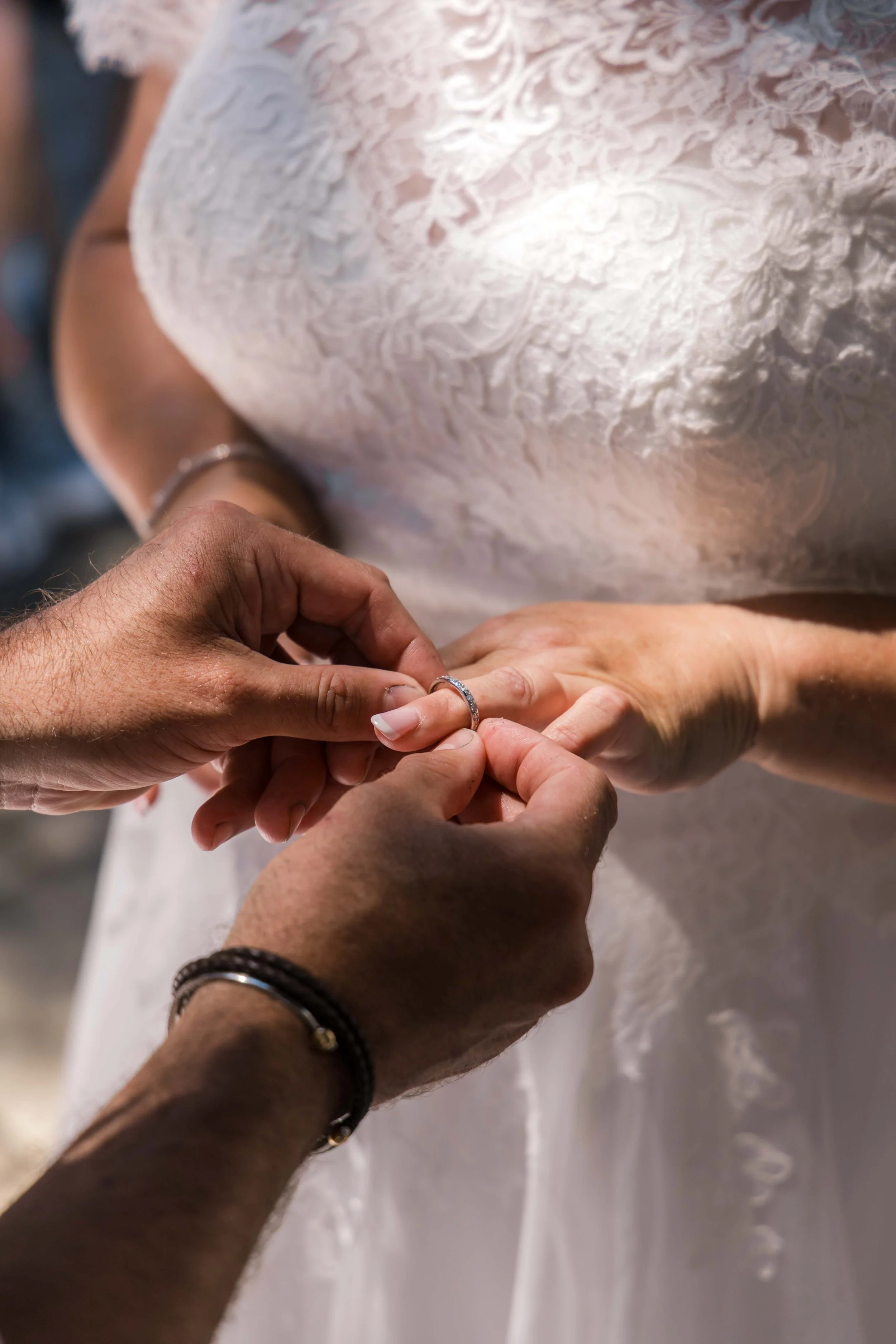 Person is placing a wedding ring on a woman's finger during a wedding ceremony.