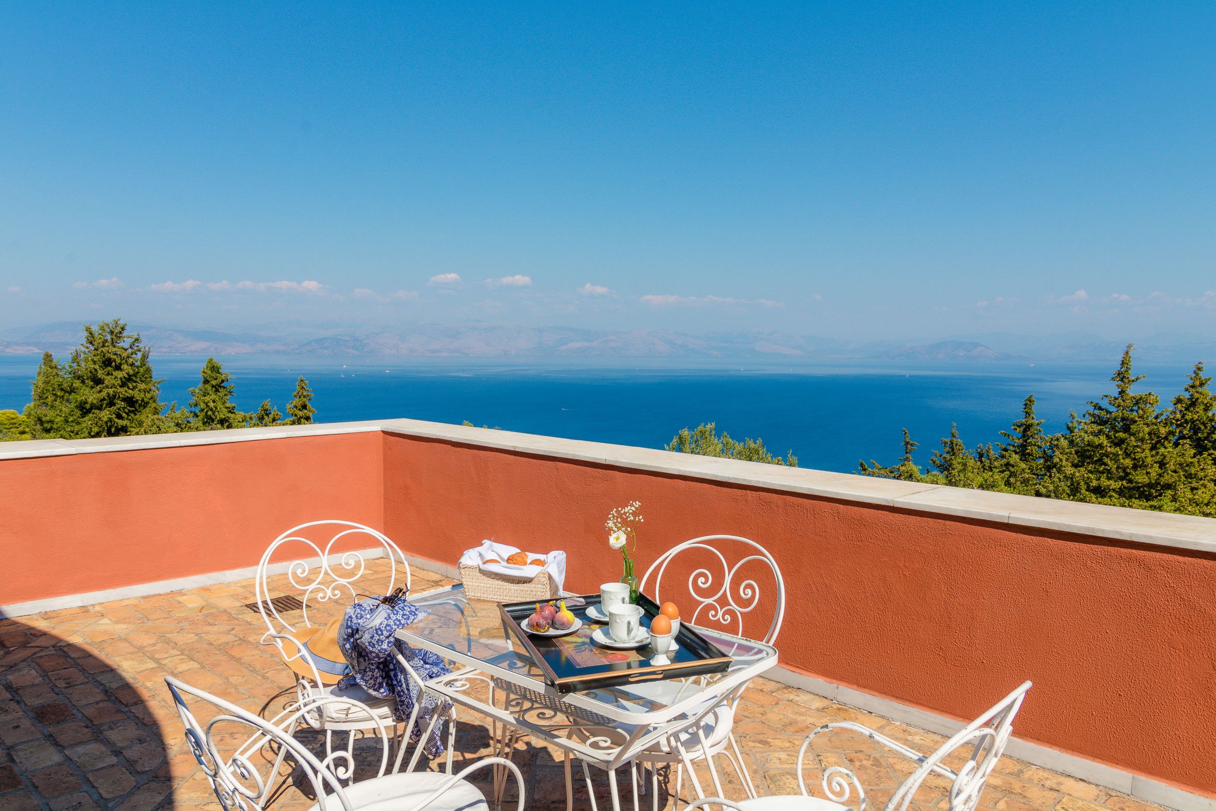 A patio with a table set for breakfast, overlooking a large lake with mountains in the background and a clear blue sky.