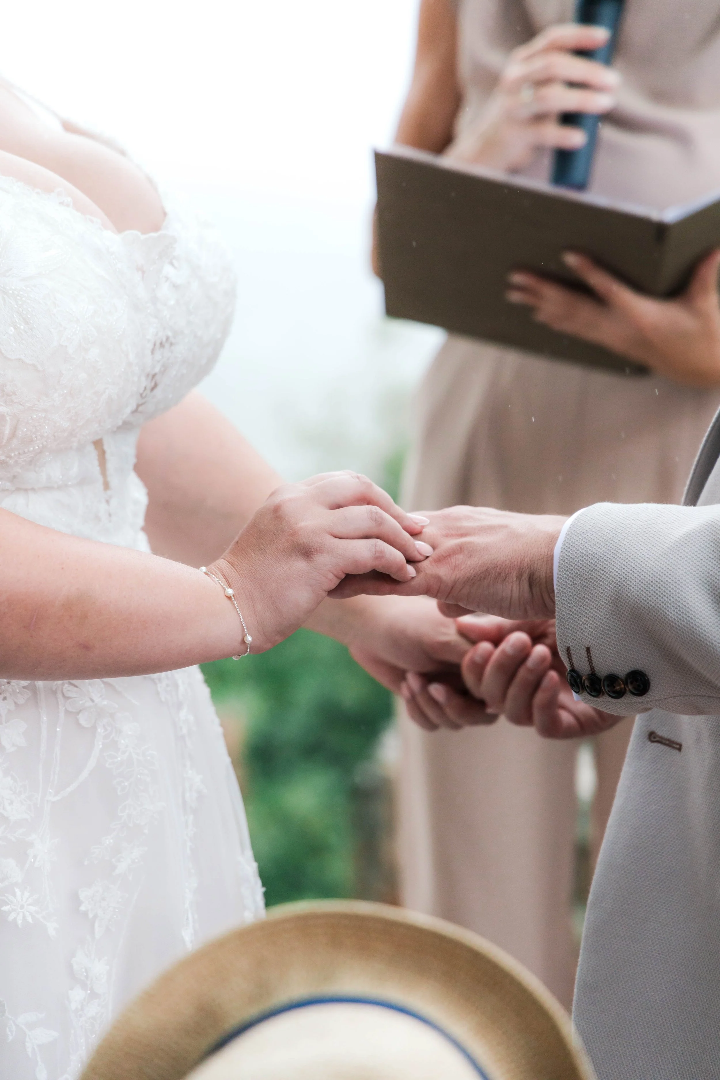 Close-up of a wedding ceremony where the bride and groom hold hands during the vows, with the officiant reading from a book in the background.