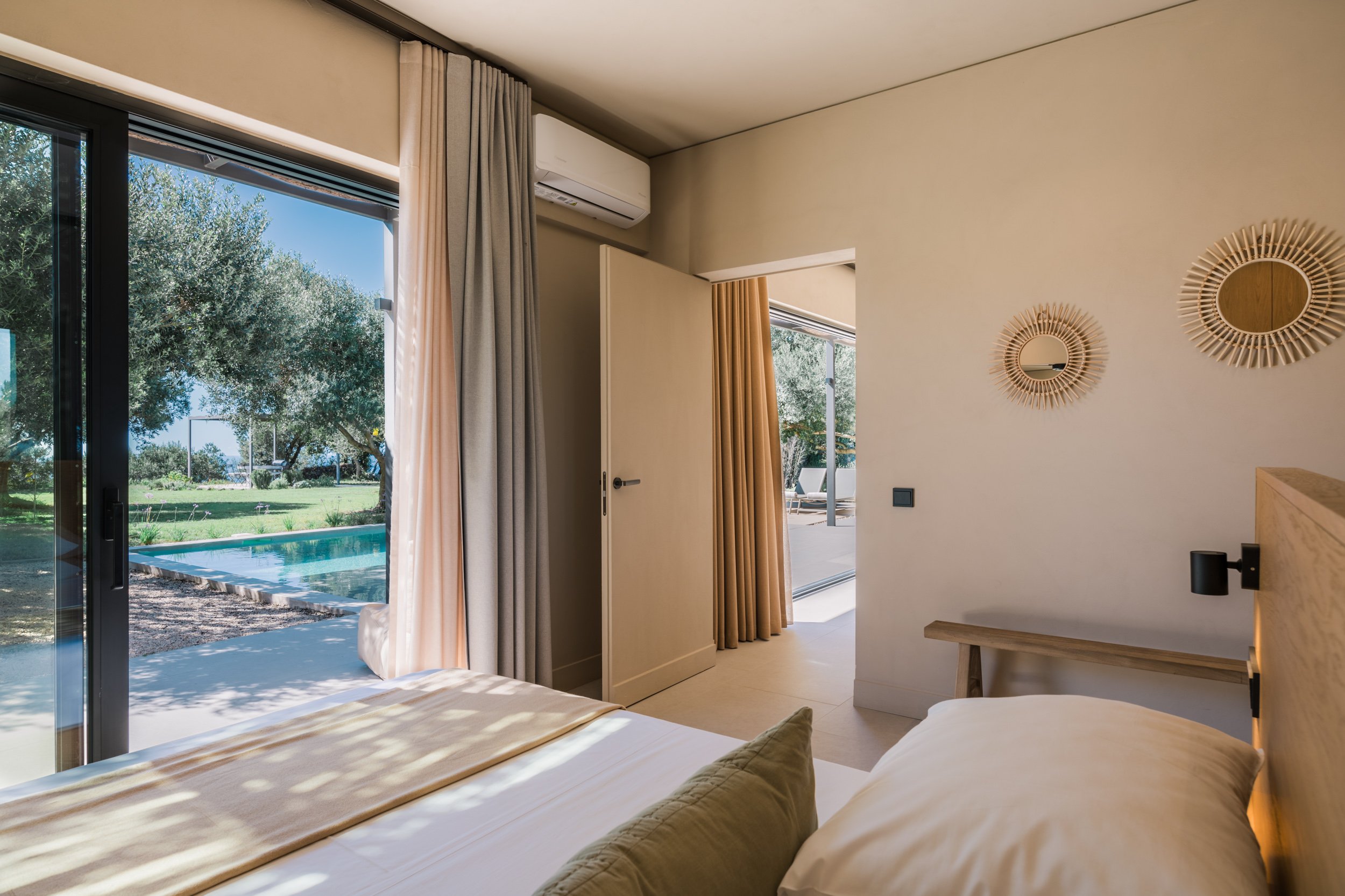A bedroom with a sliding glass door opening to a patio with a pool and green yard, beige walls, and wooden decor.